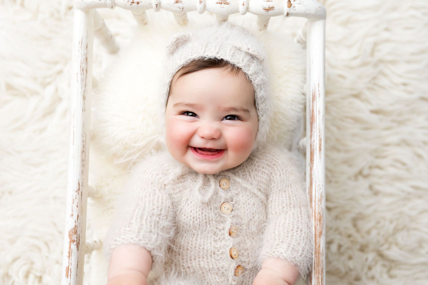 Baby wearing knit outfit posing in rustic white crate.