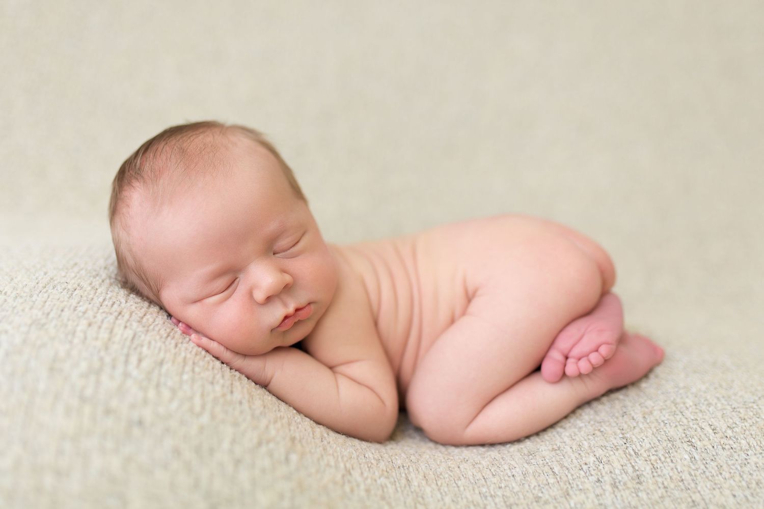 Peaceful sleeping newborn photographed on neutral beige background.