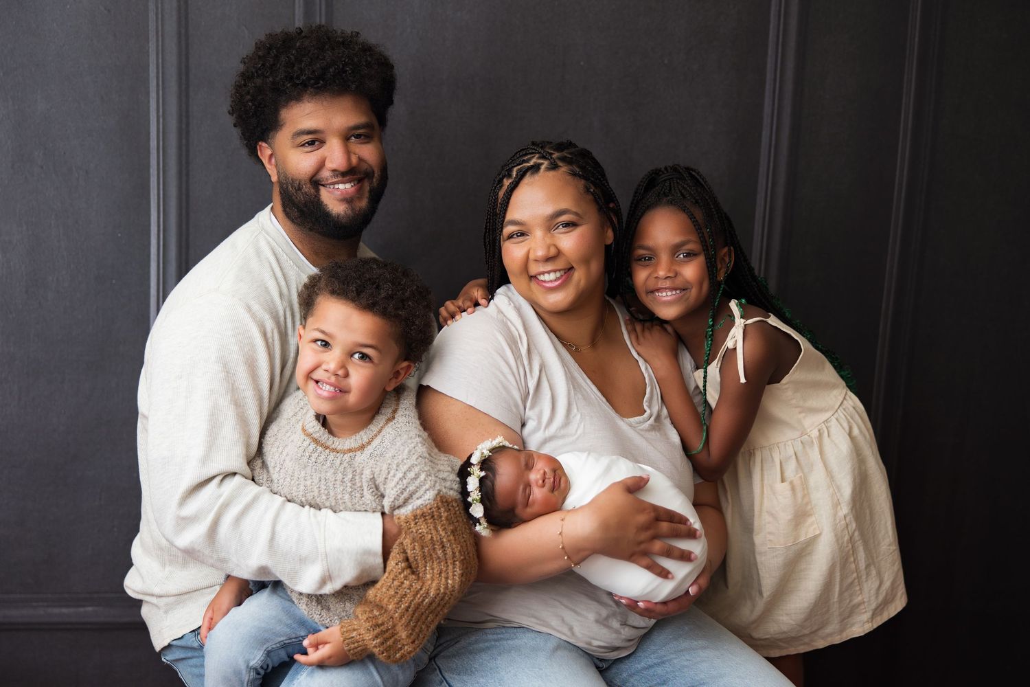 Happy family portrait with newborn baby against dark backdrop.