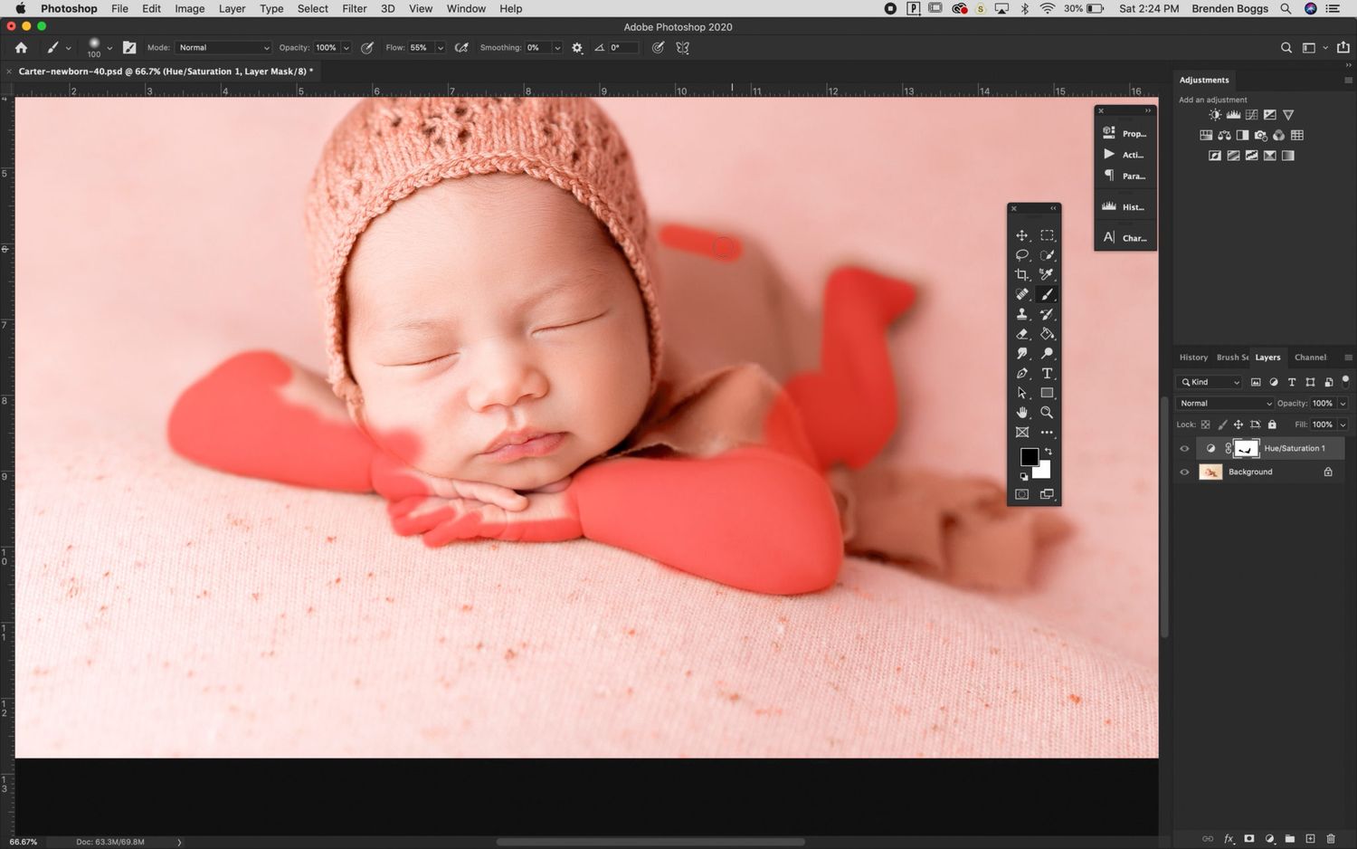 A sleeping newborn wearing a knit hat rests on a pink blanket with red heart-shaped decorations.