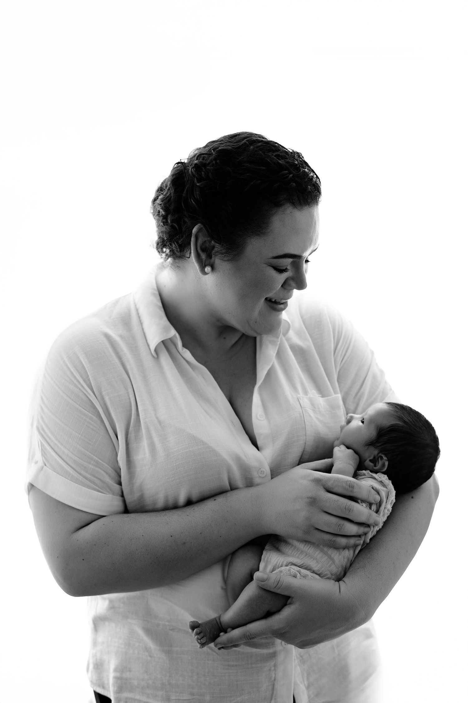 A tender black and white portrait of a mother in white clothing holding and gazing lovingly at her newborn baby.