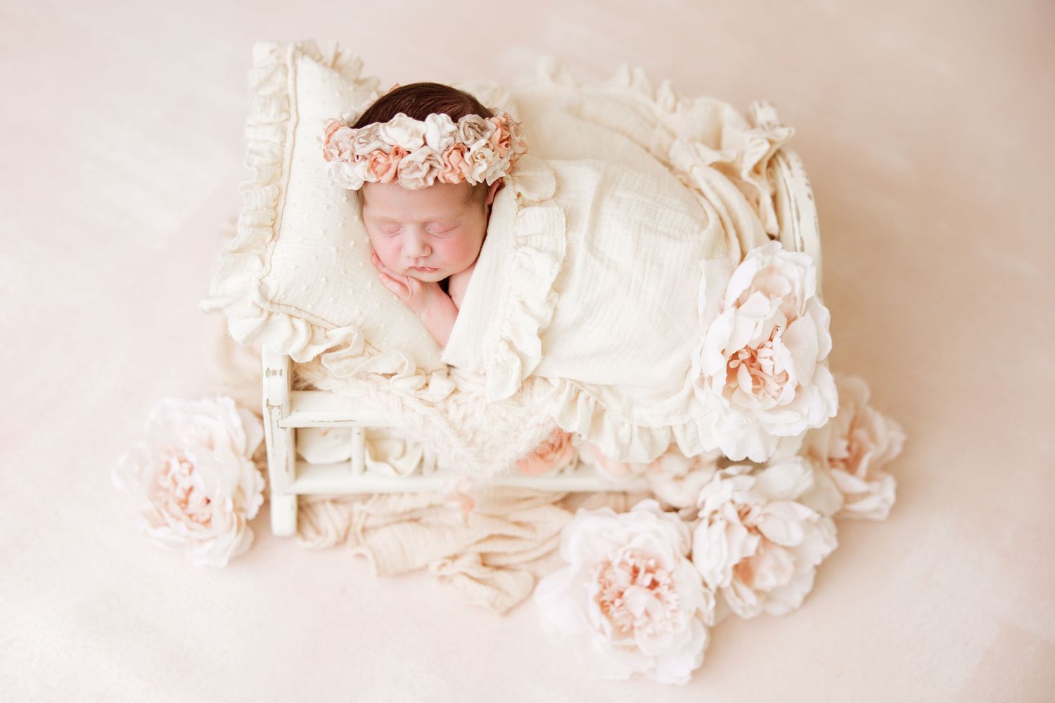Series of peaceful newborn photos with delicate pink floral arrangements and white fabrics.