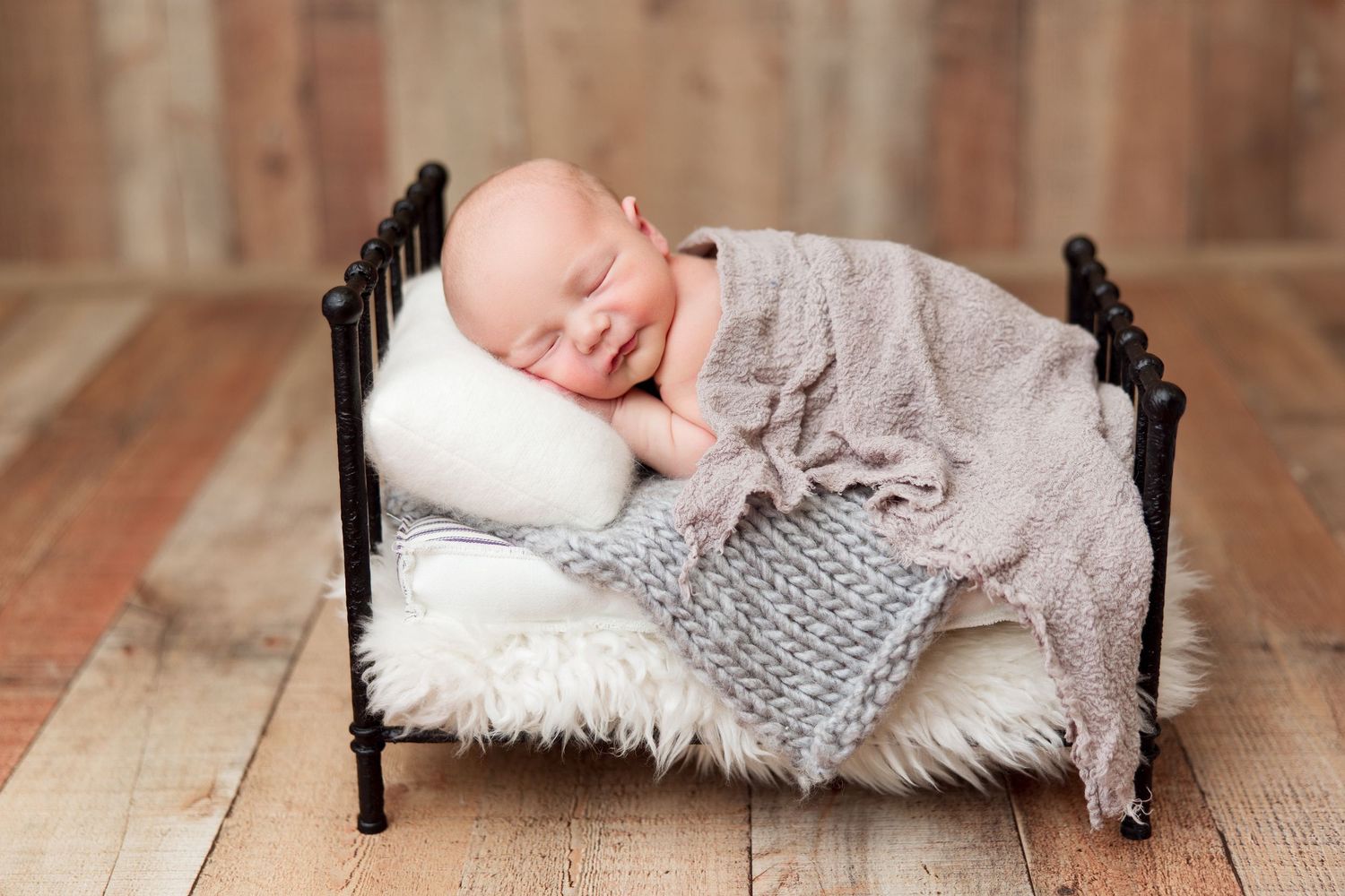 Newborn sleeping on antique miniature bed with knitted blanket.