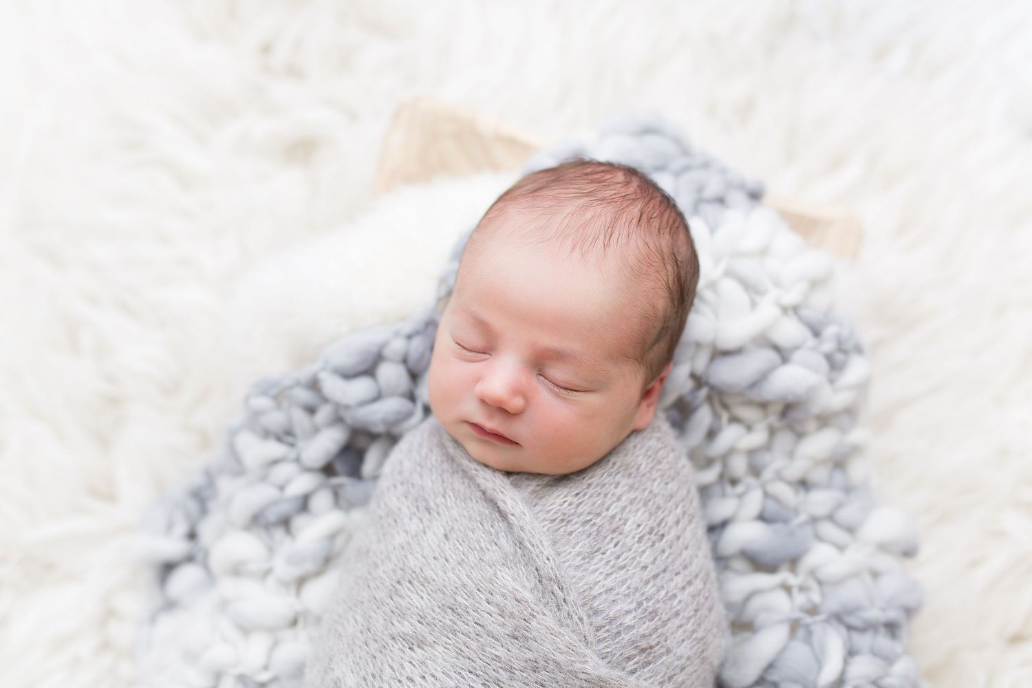 Sleeping newborn baby wrapped in soft gray blanket on white textured background.