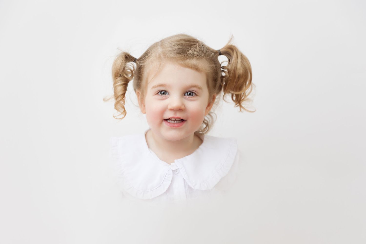 Sweet portrait of a toddler with pigtails and a white dress against a light background. heirloom portrait