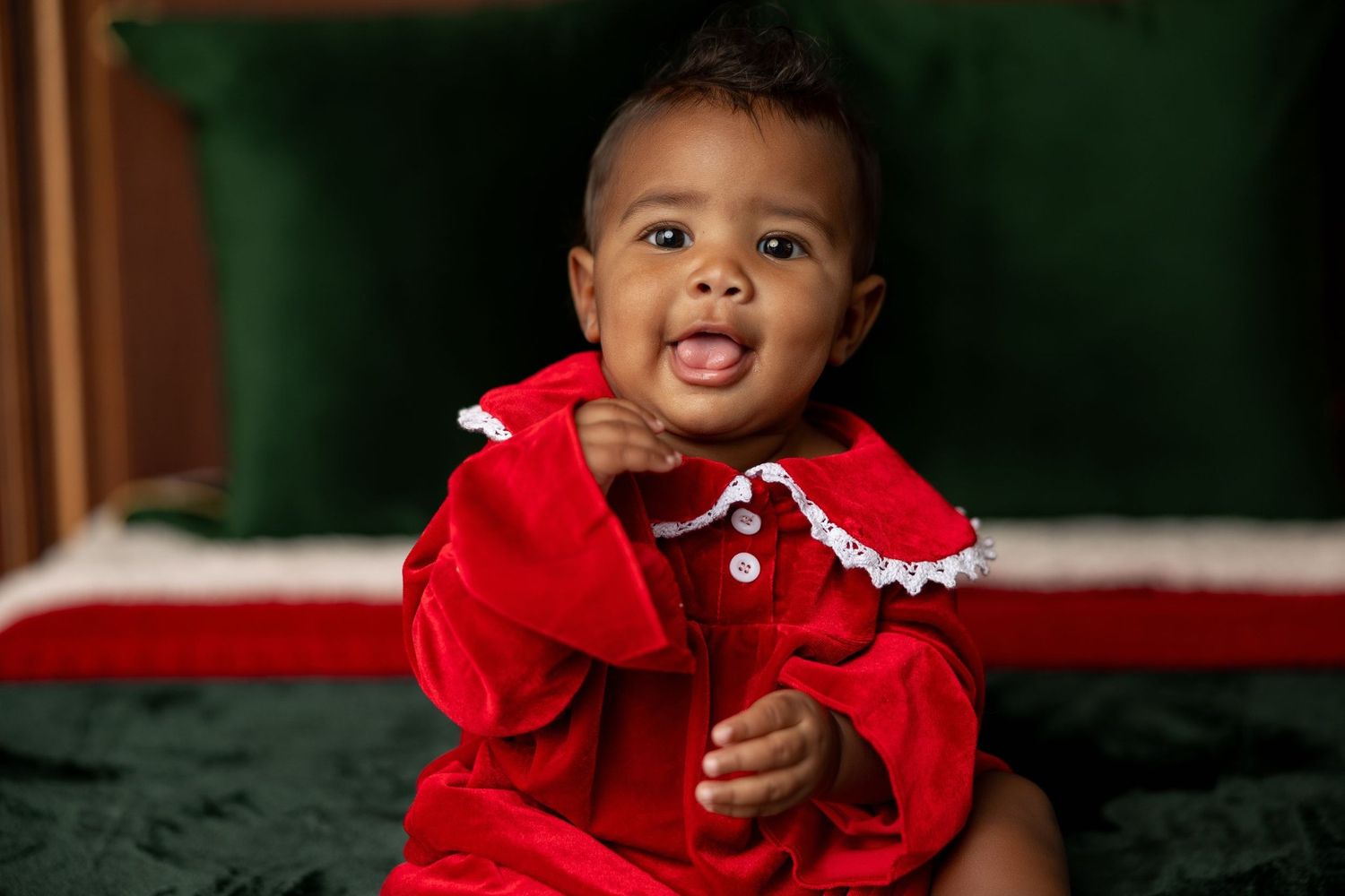 Smiling baby in a red velvet holiday dress at a Milk & Cookies Christmas mini session in Pacific Grove