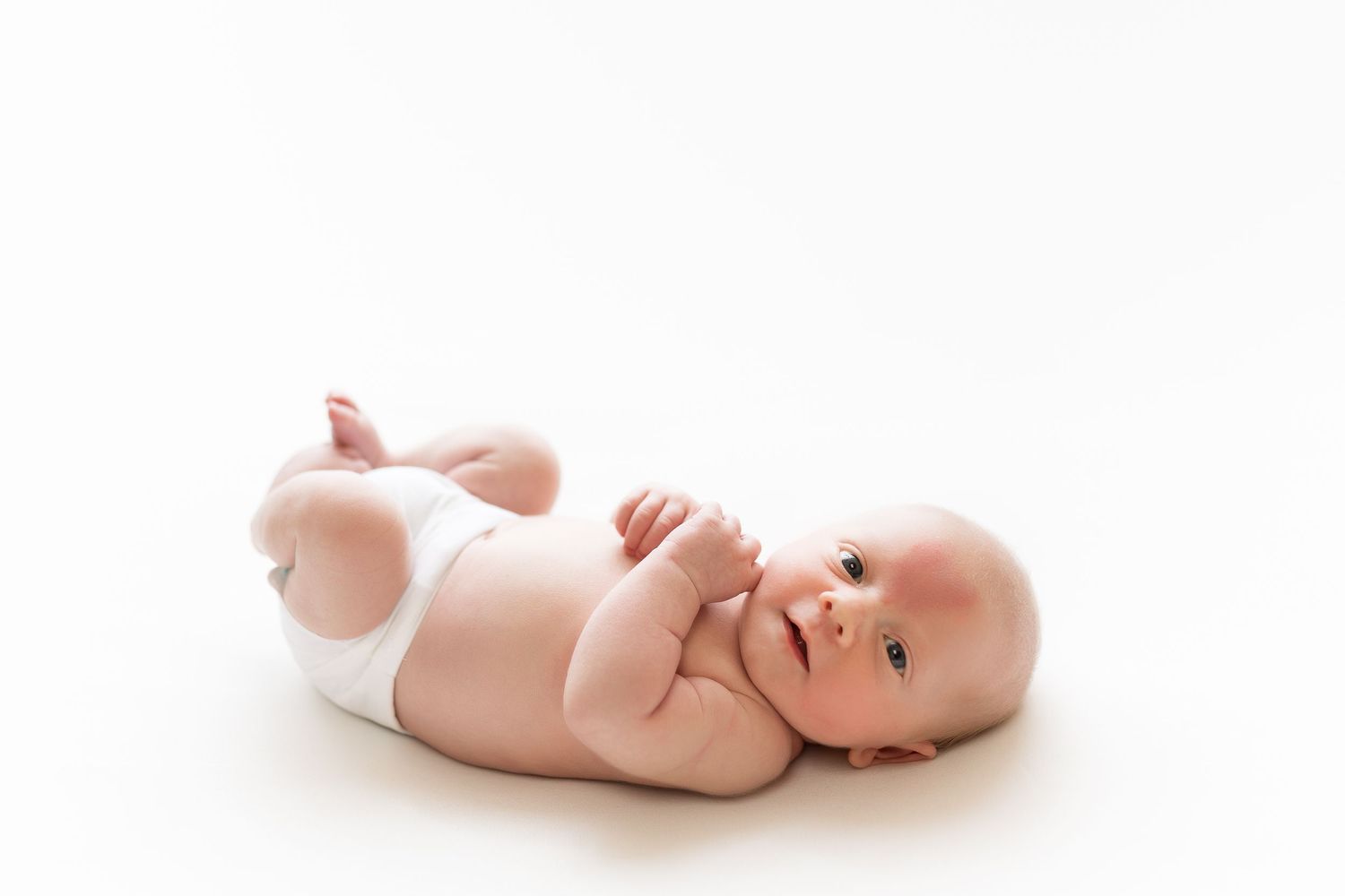 Baby wearing white diaper laying on back against white backdrop.