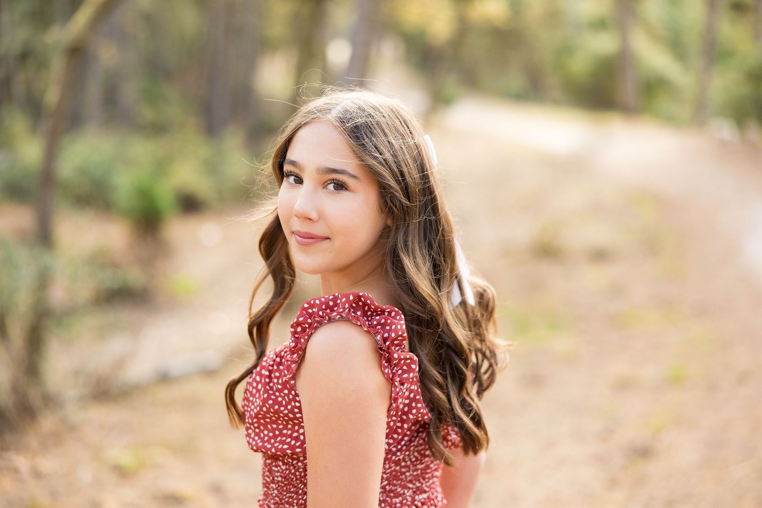 Portrait of a person in red dress turning to smile over their shoulder in a wooded setting.