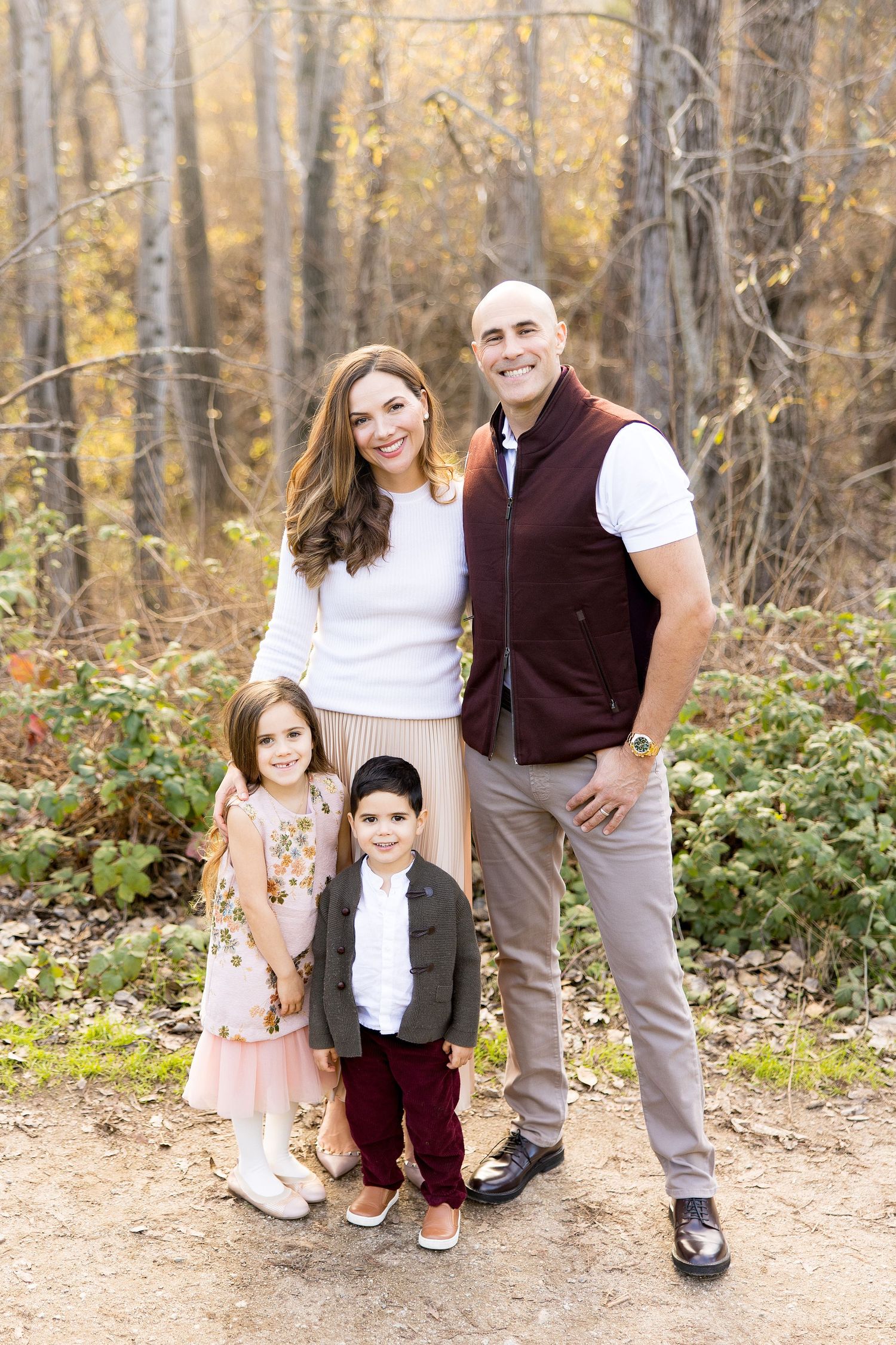 Family of four in coordinating autumn outfits posing in wooded setting.