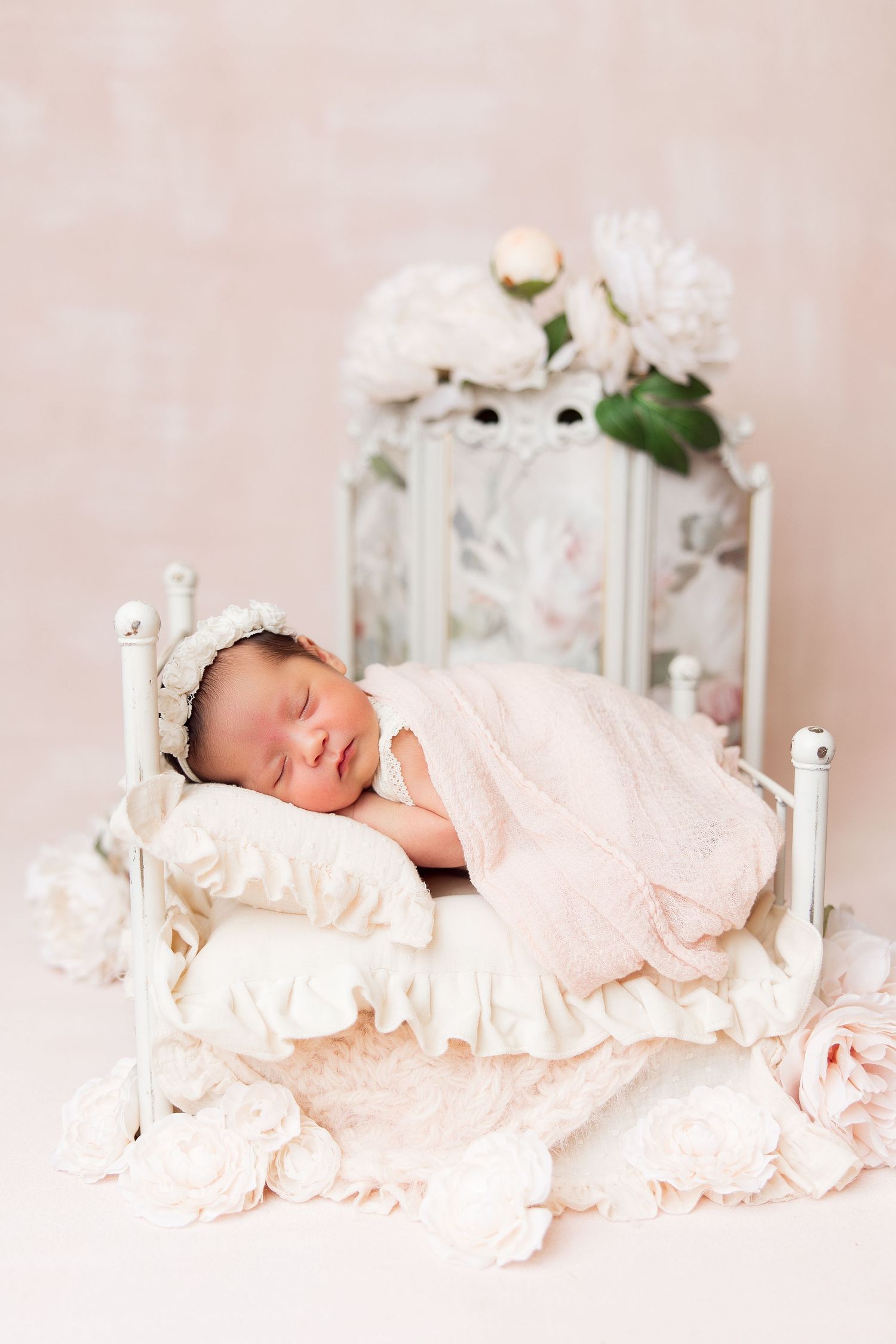Newborn sleeping peacefully in vintage white bed with roses and floral decor.
