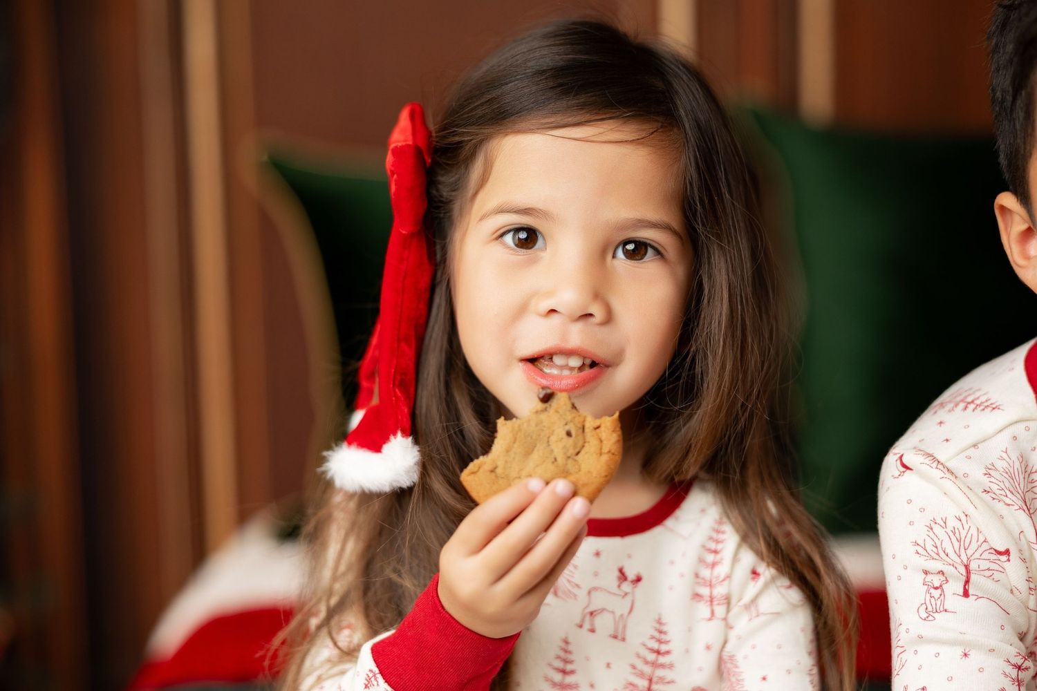 Girl in a Santa hat and Christmas pajamas eating a cookie at a Milk & Cookies holiday mini session in Pacific Grove