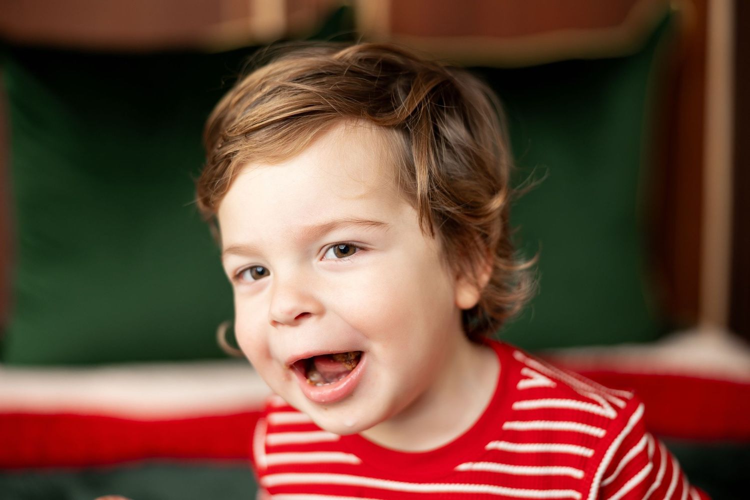 Happy toddler boy in red and white striped Christmas pajamas at a Milk & Cookies holiday mini session in Pacific Grove