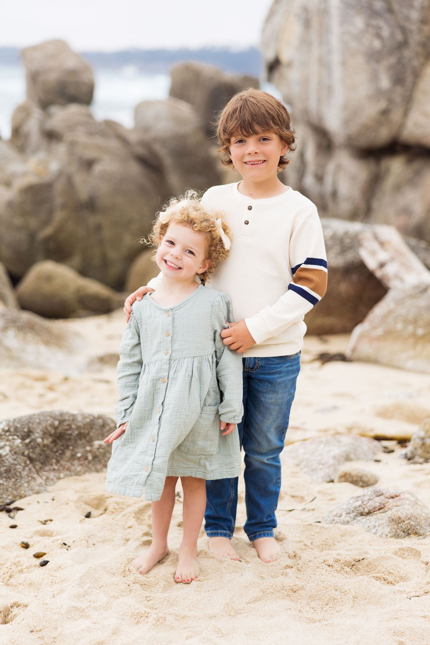 Children playing on rocky beach during sunset photoshoot.