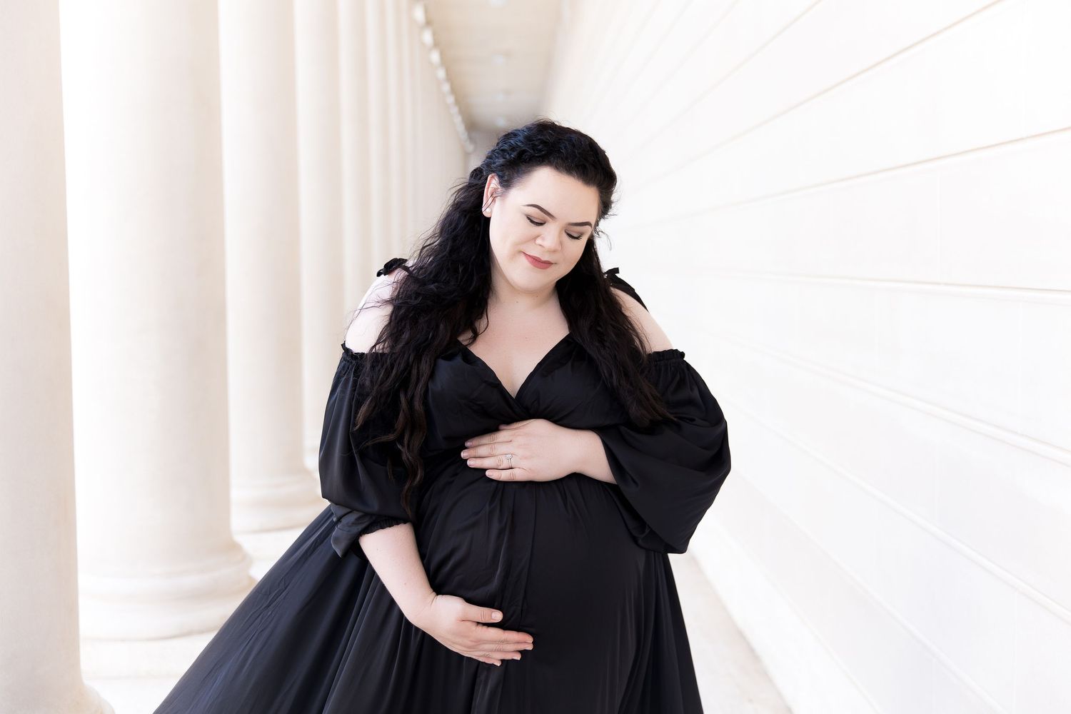 Elegant black dress portrait session against white columns in classic architectural setting.