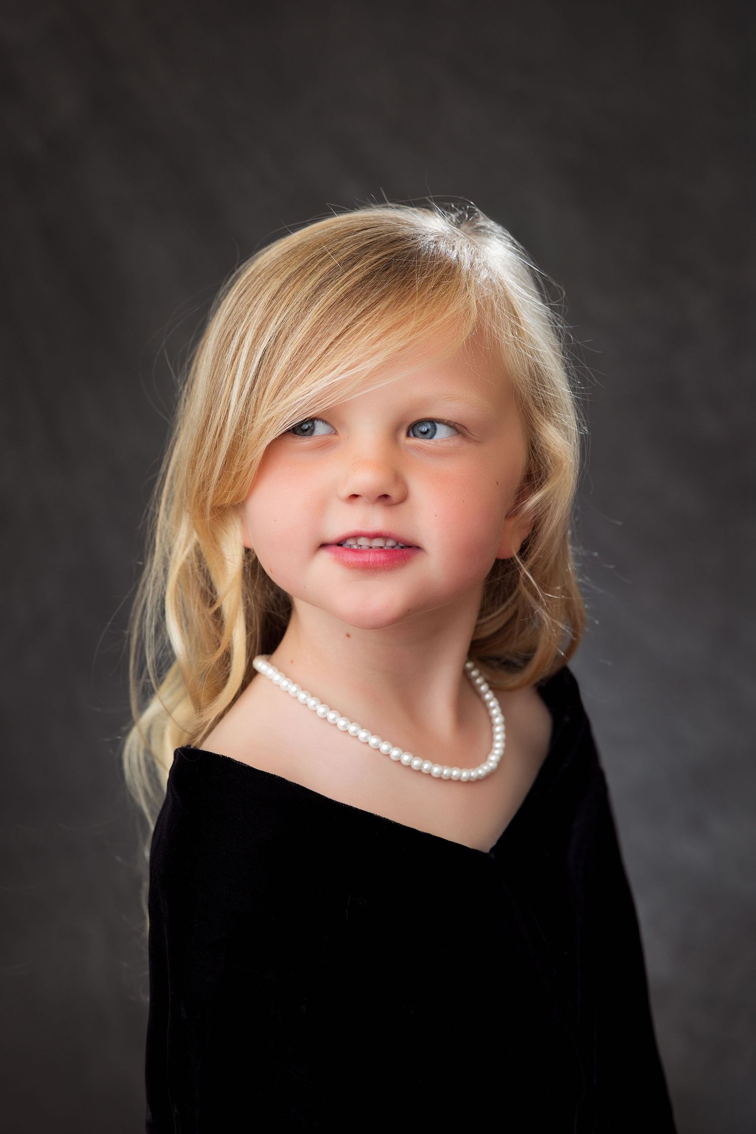 A series of four professional black and white portrait photographs showing a child wearing a pearl necklace and dark clothing.