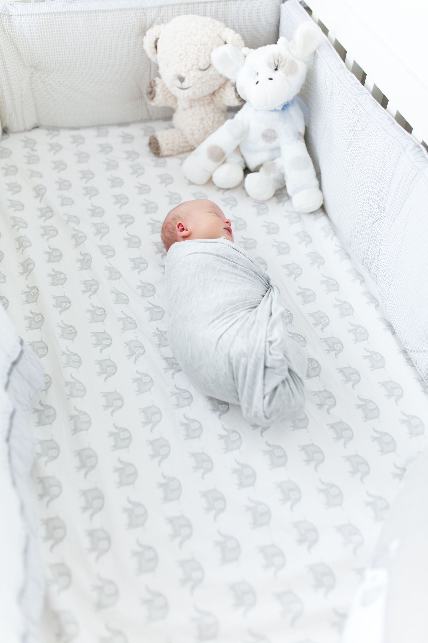 White crib with elephant print bedding and plush animal toys in a neutral nursery, lifestyle newborn session