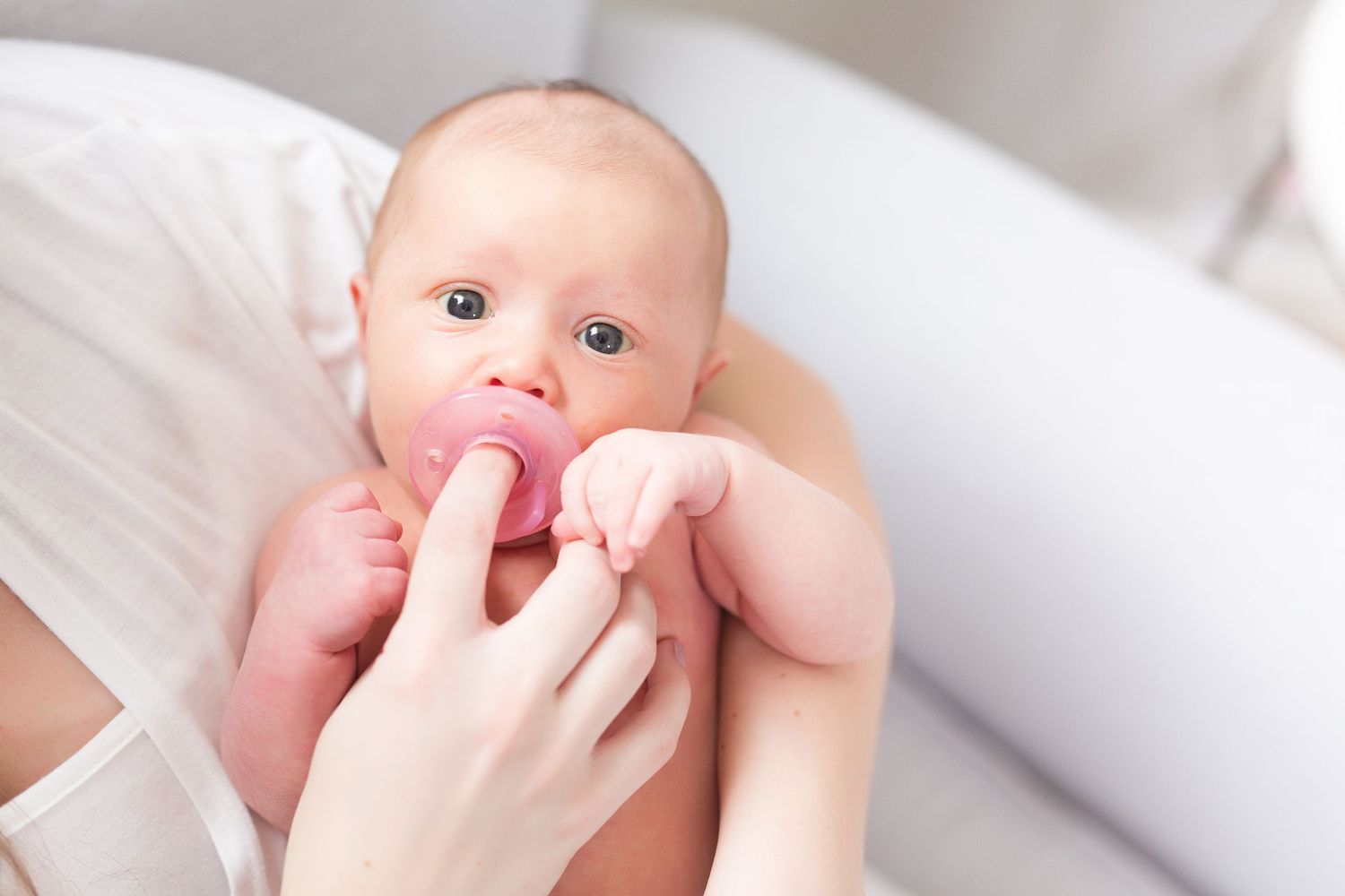 Close up of baby sucking on pink pacifier with hands visible.