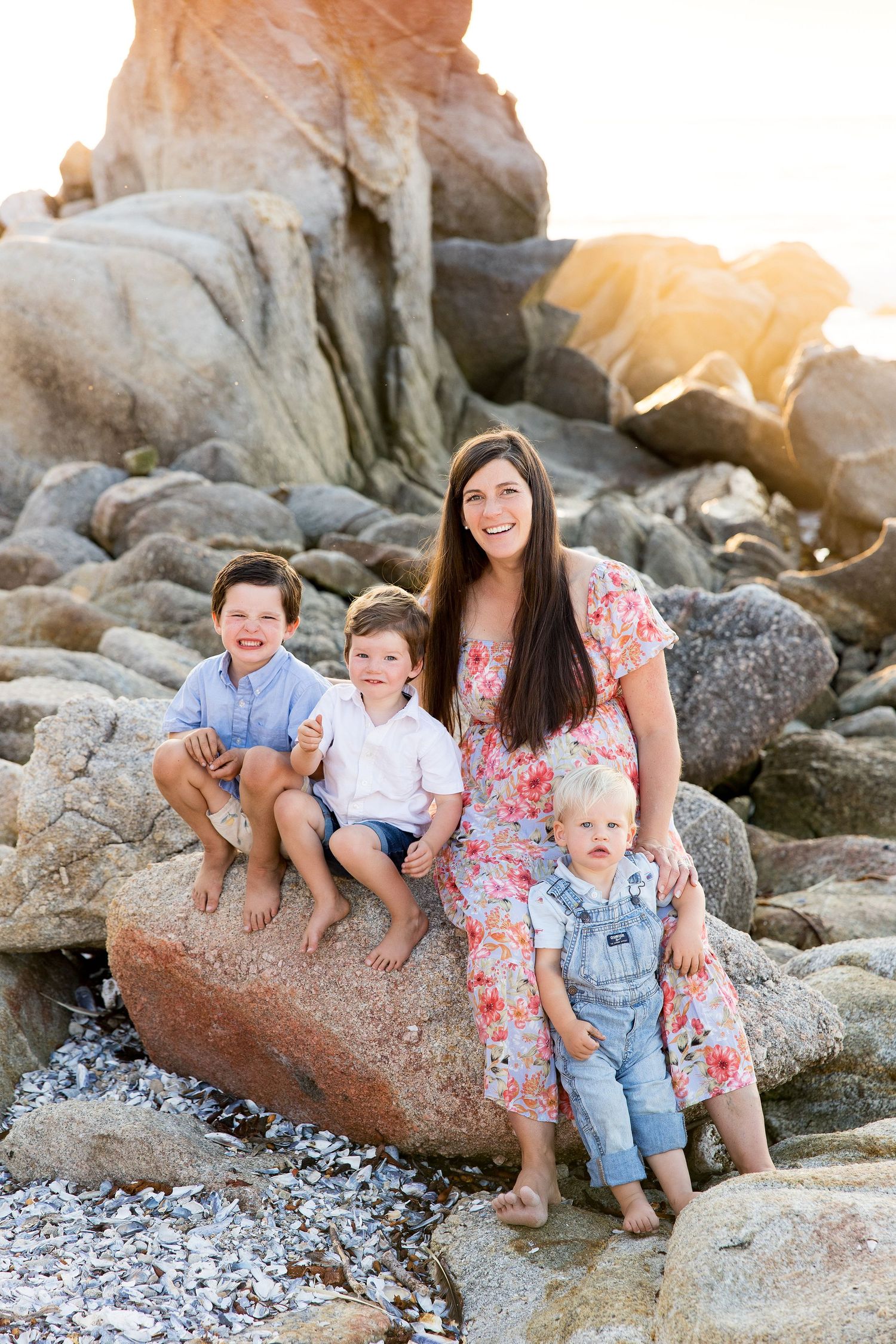 A family sits together on coastal rocks during a beach photoshoot in casual attire.