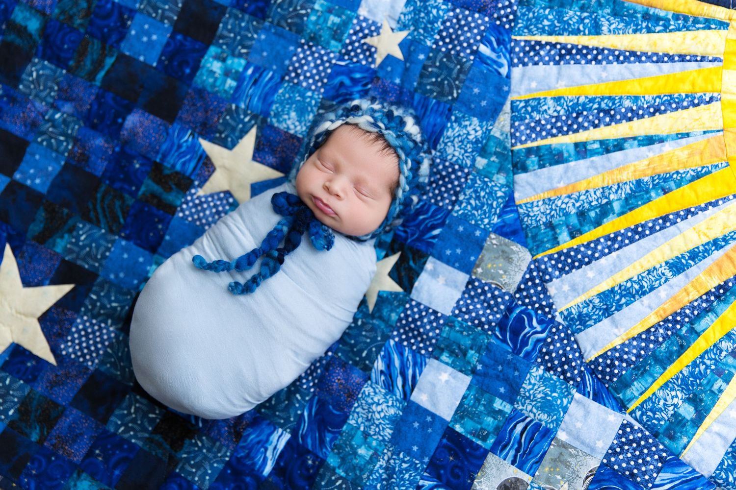 Baby lying on blue and white star-patterned blanket with patriotic American flag themed decorations.