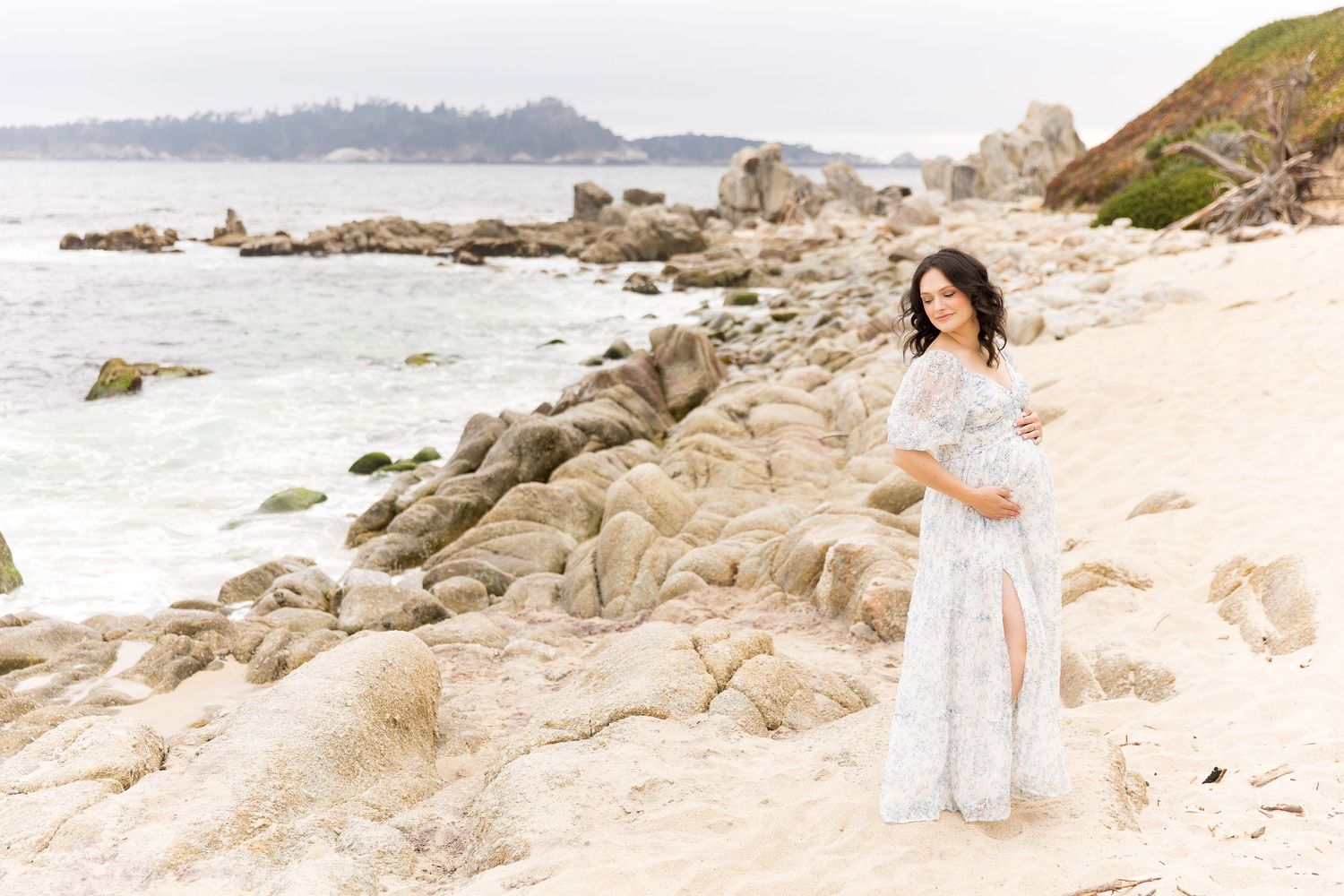 Maternity photo session on scenic rocky beach with ocean waves and coastal views.
