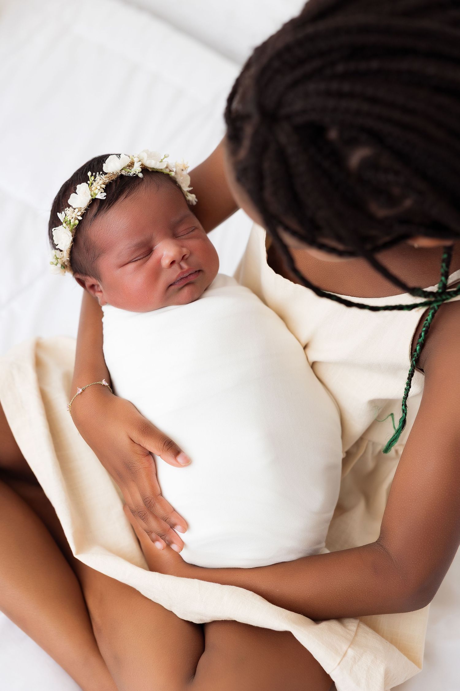 Sleeping newborn wearing floral crown wrapped in white swaddle.