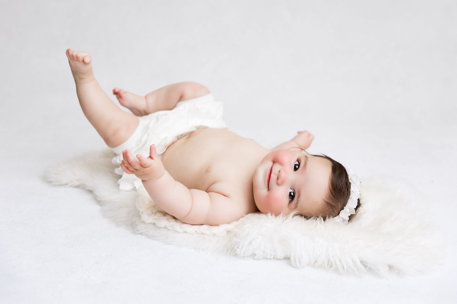 Happy baby resting on plush white blanket in studio setting.