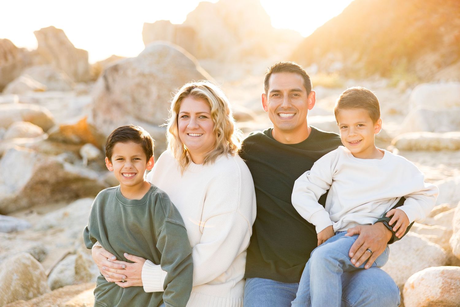 A series of relaxed family portraits on rocks by the ocean at sunset.