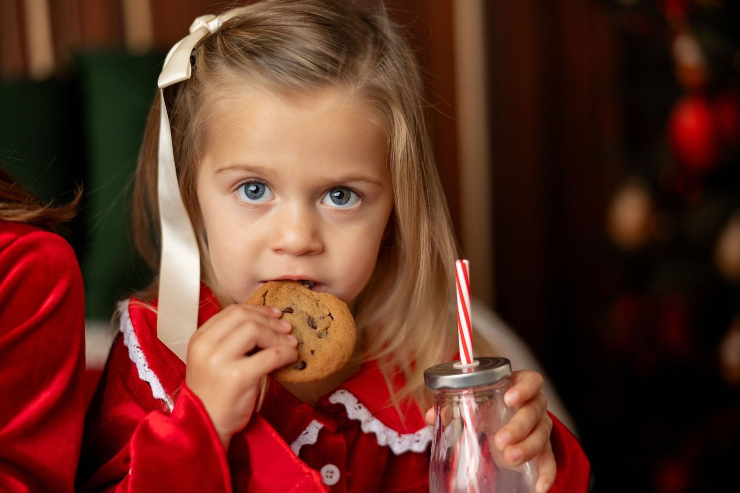 Girl in a red dress eating a cookie with a milk jar and straw at a Christmas mini session in Pacific Grove