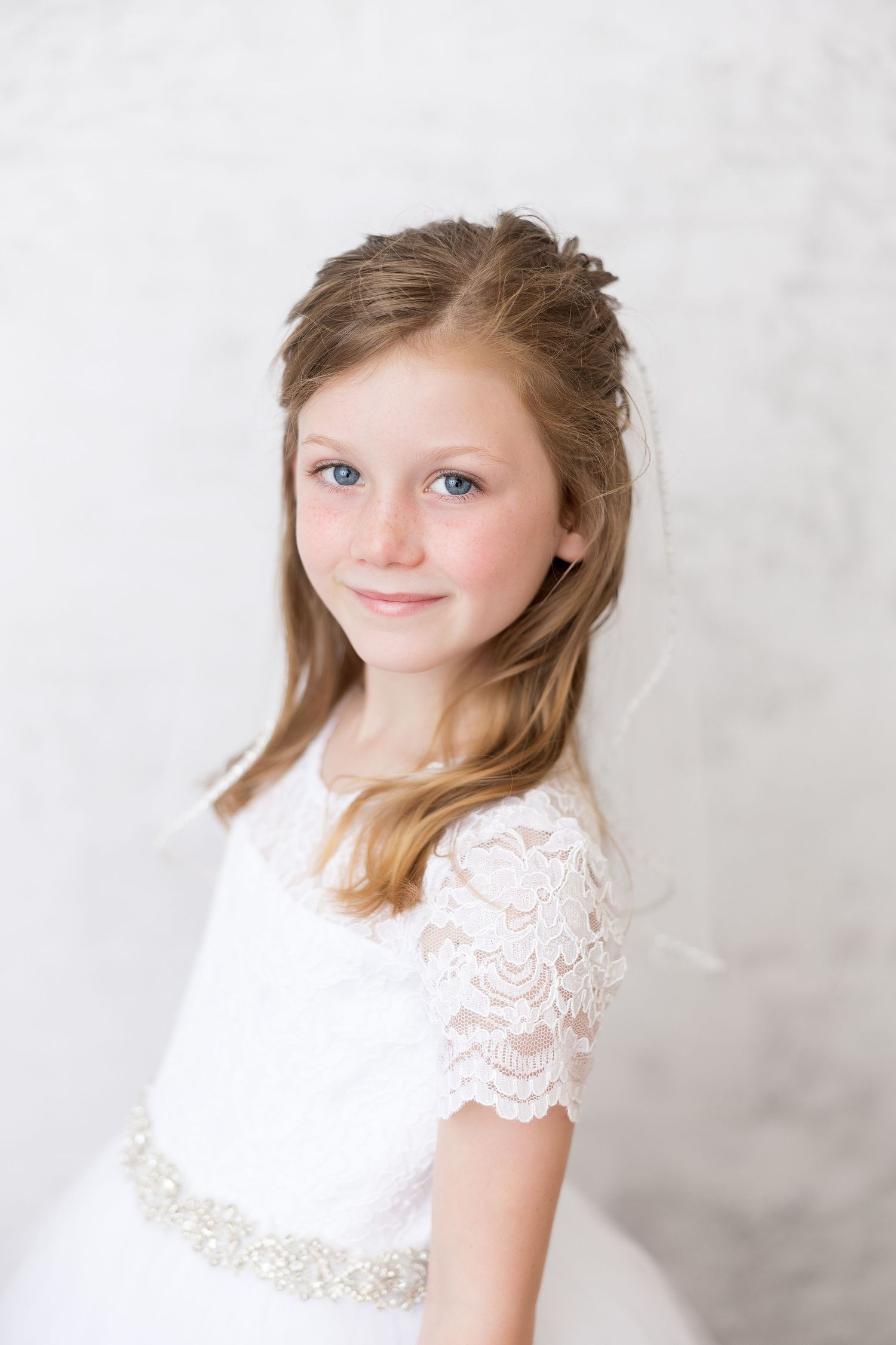 A portrait in an elegant white lace dress with beaded waistband against a light backdrop.