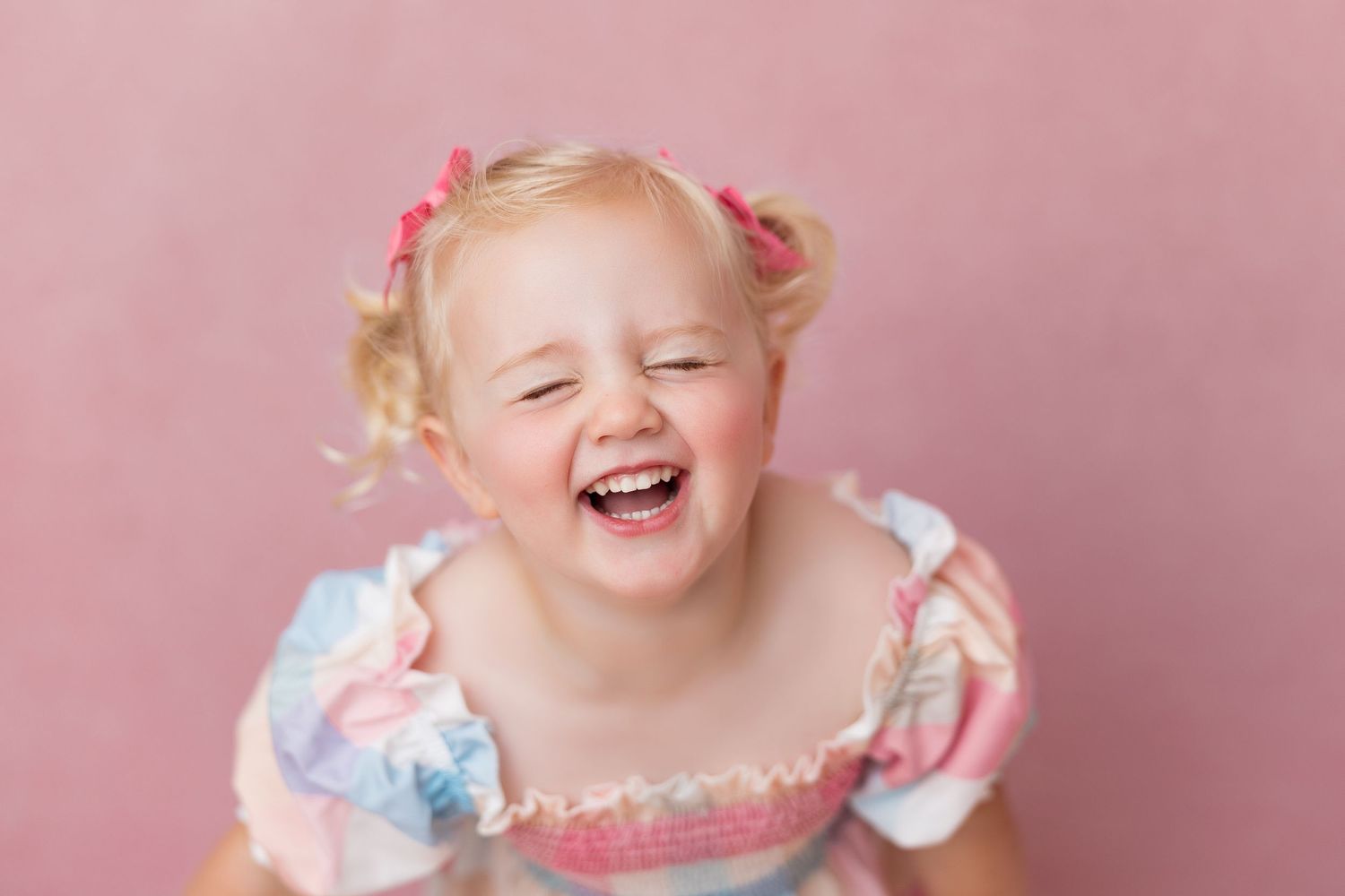 A collage of four photos showing a joyful baby in a pink dress with ruffles against a pink backdrop.