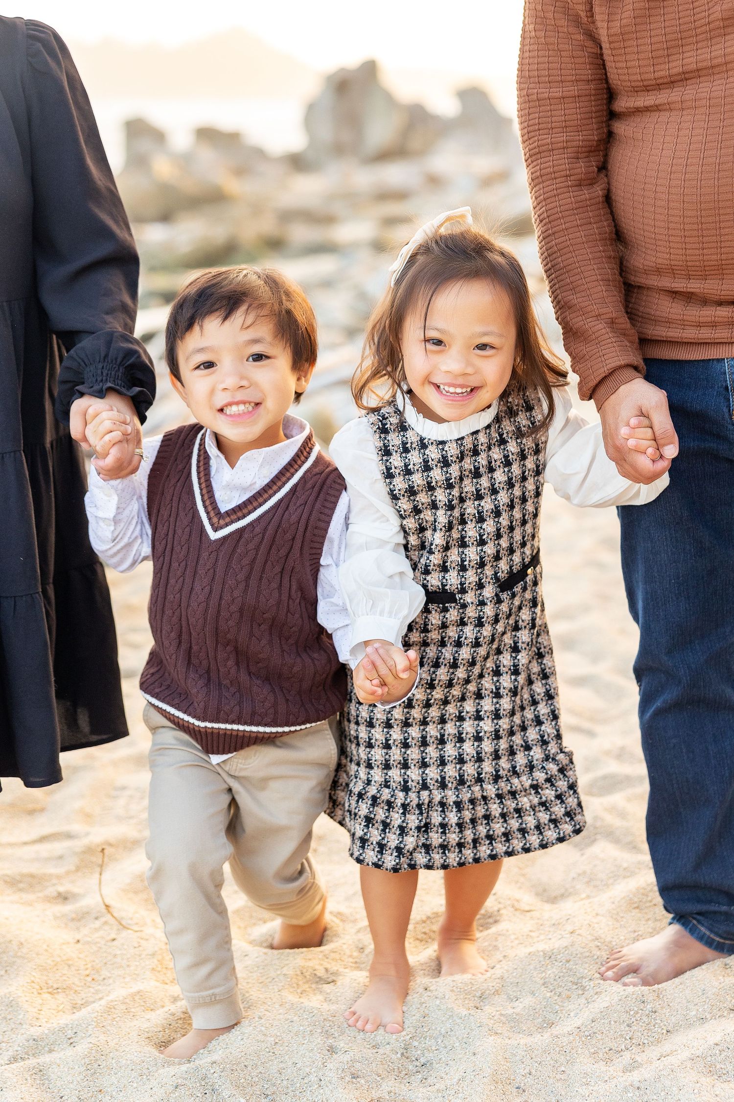 Children holding hands while walking on sandy beach with parents.