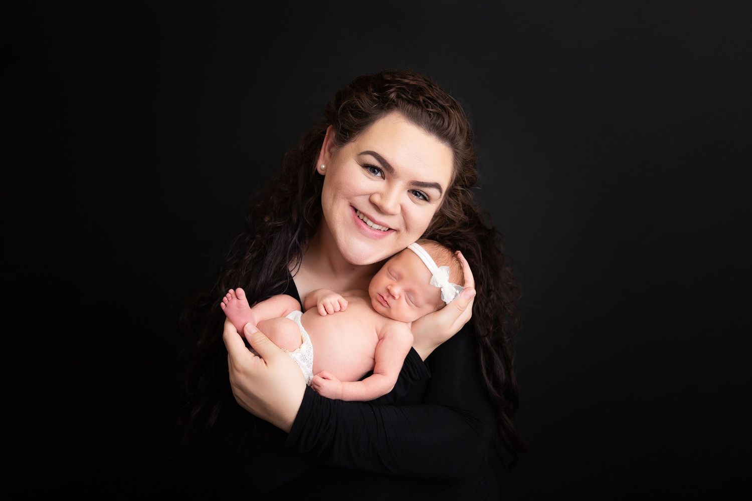 A tender newborn photography portrait against a dark background.