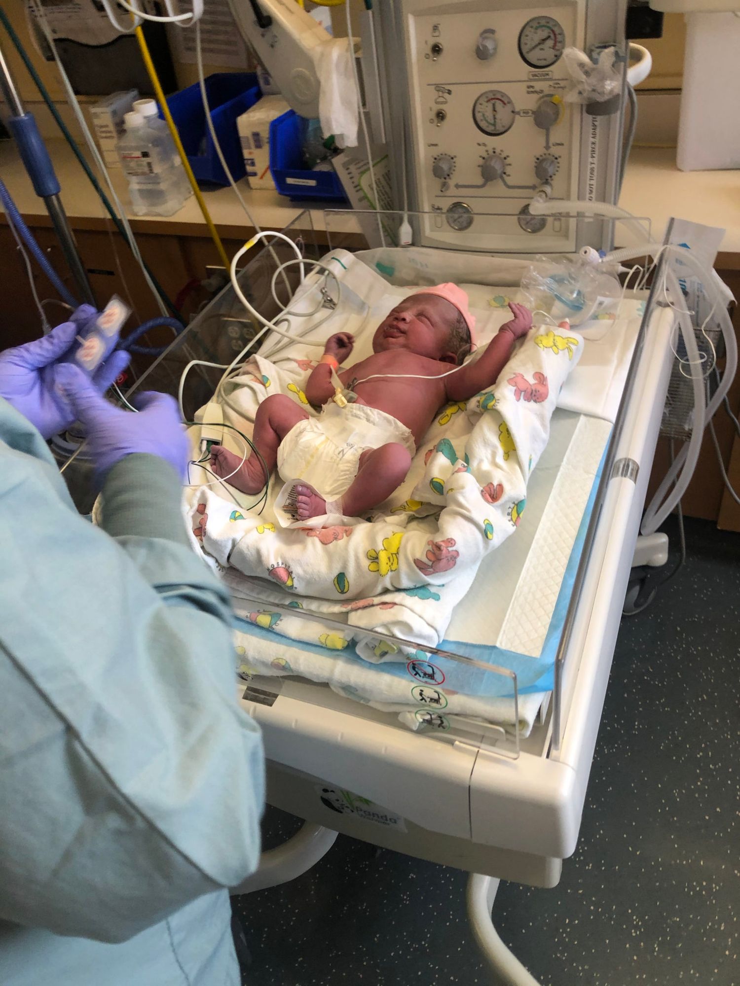 Medical staff care for a newborn baby in a hospital nursery incubator with monitoring equipment.