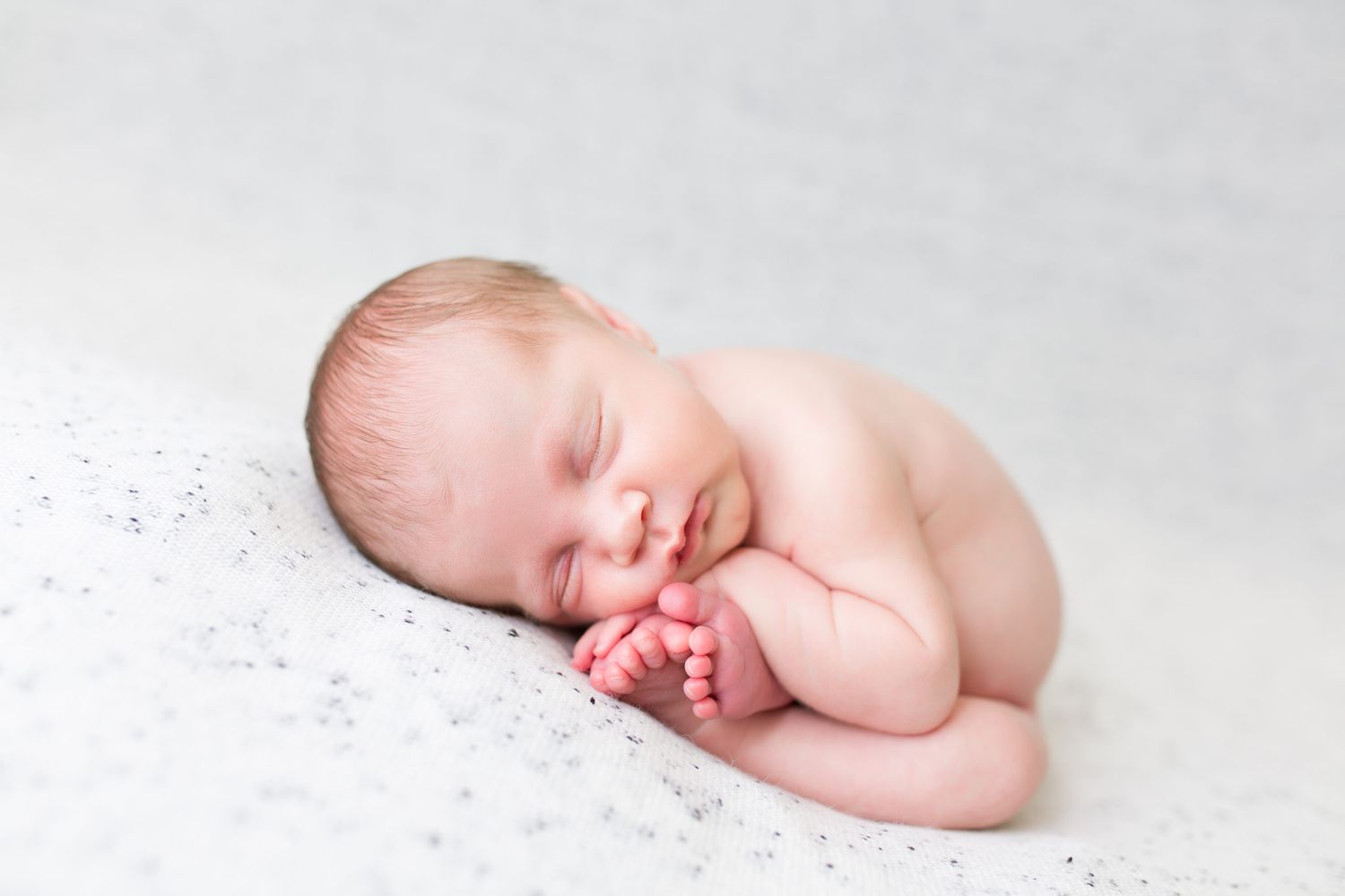 A sleeping newborn baby curled up in a peaceful pose on a soft white blanket.
