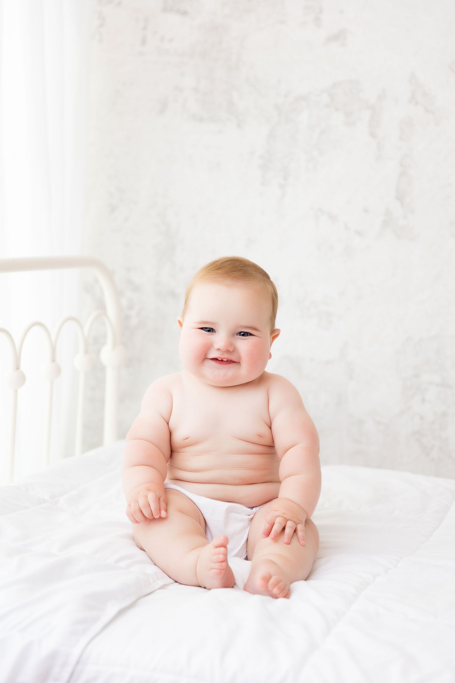 chunky 6 month old baby boy with lots of rolls on white bed in photography studio milestone session