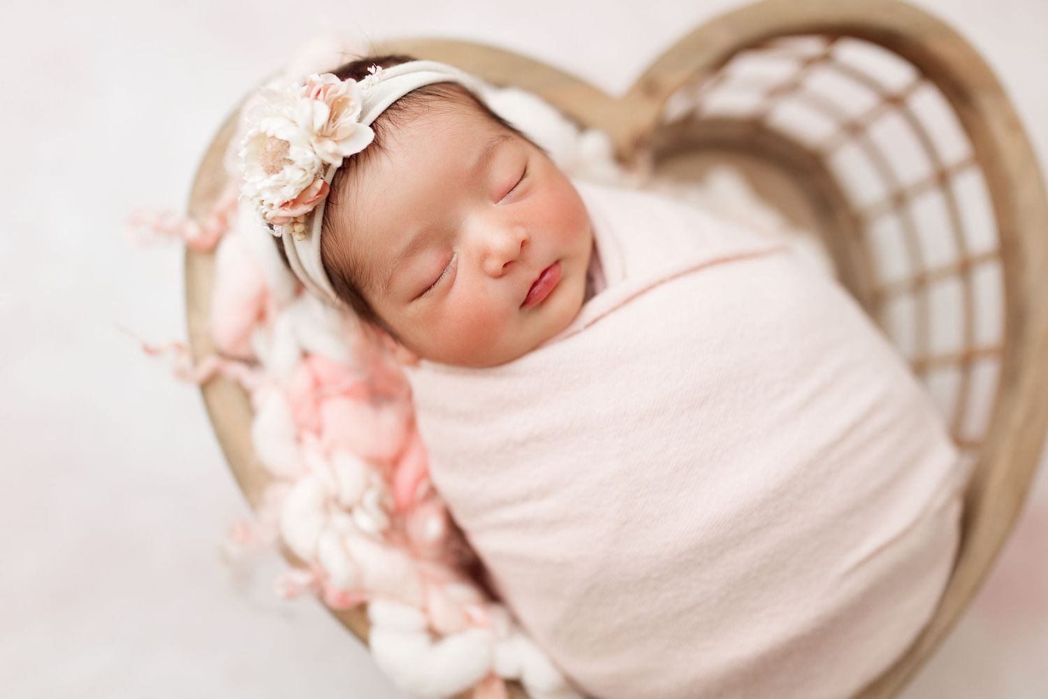 Peaceful newborn wrapped in cream fabric resting in woven basket.