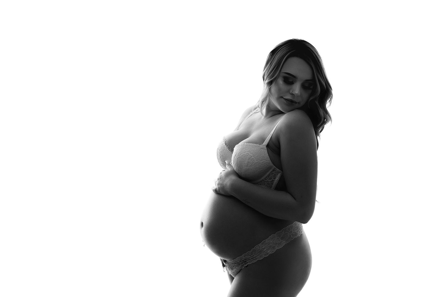 Black and white studio maternity portrait of pregnant woman in lace lingerie holding her belly