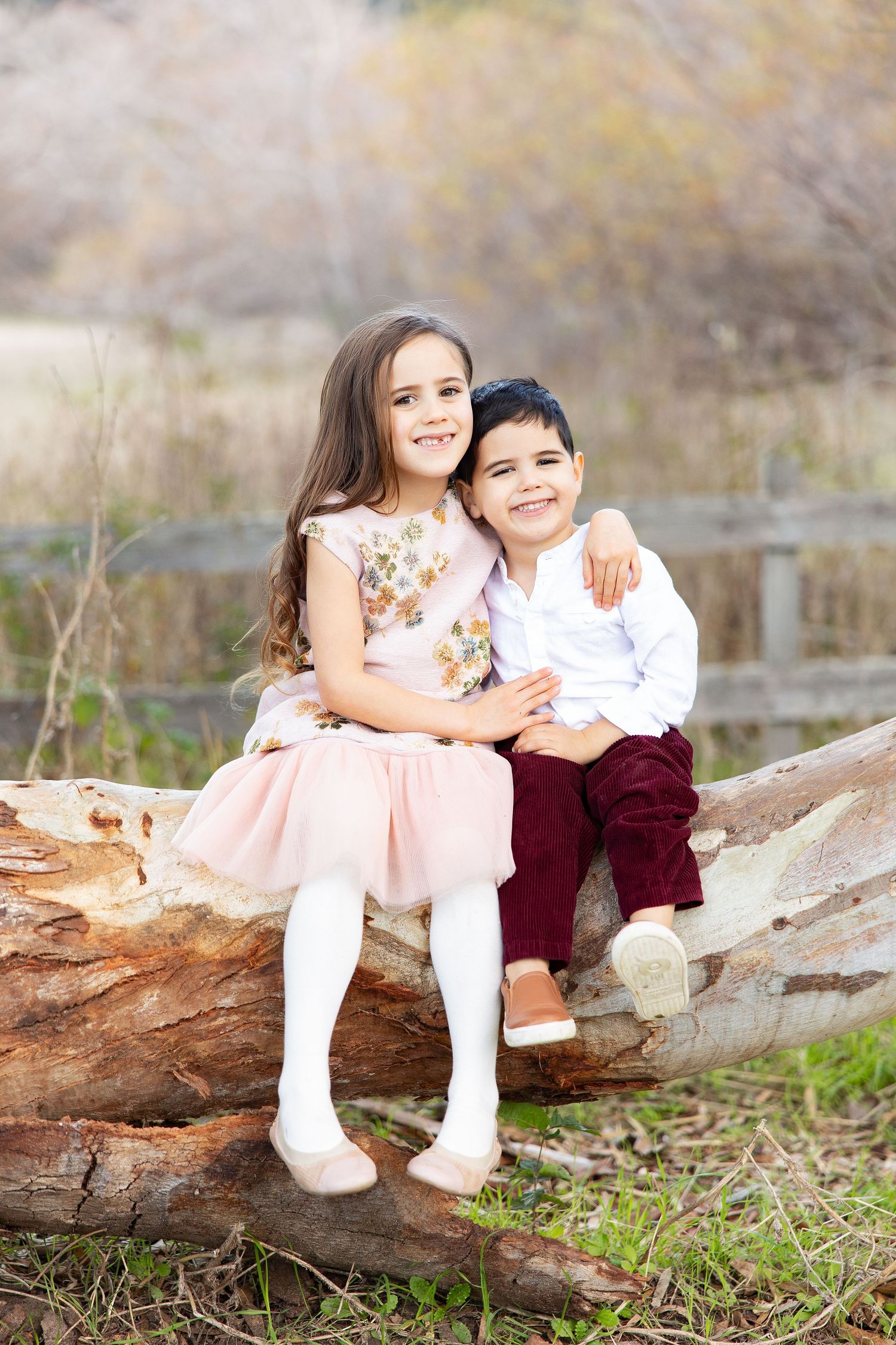 Two children share a sweet moment while sitting on a fallen tree trunk in the forest.