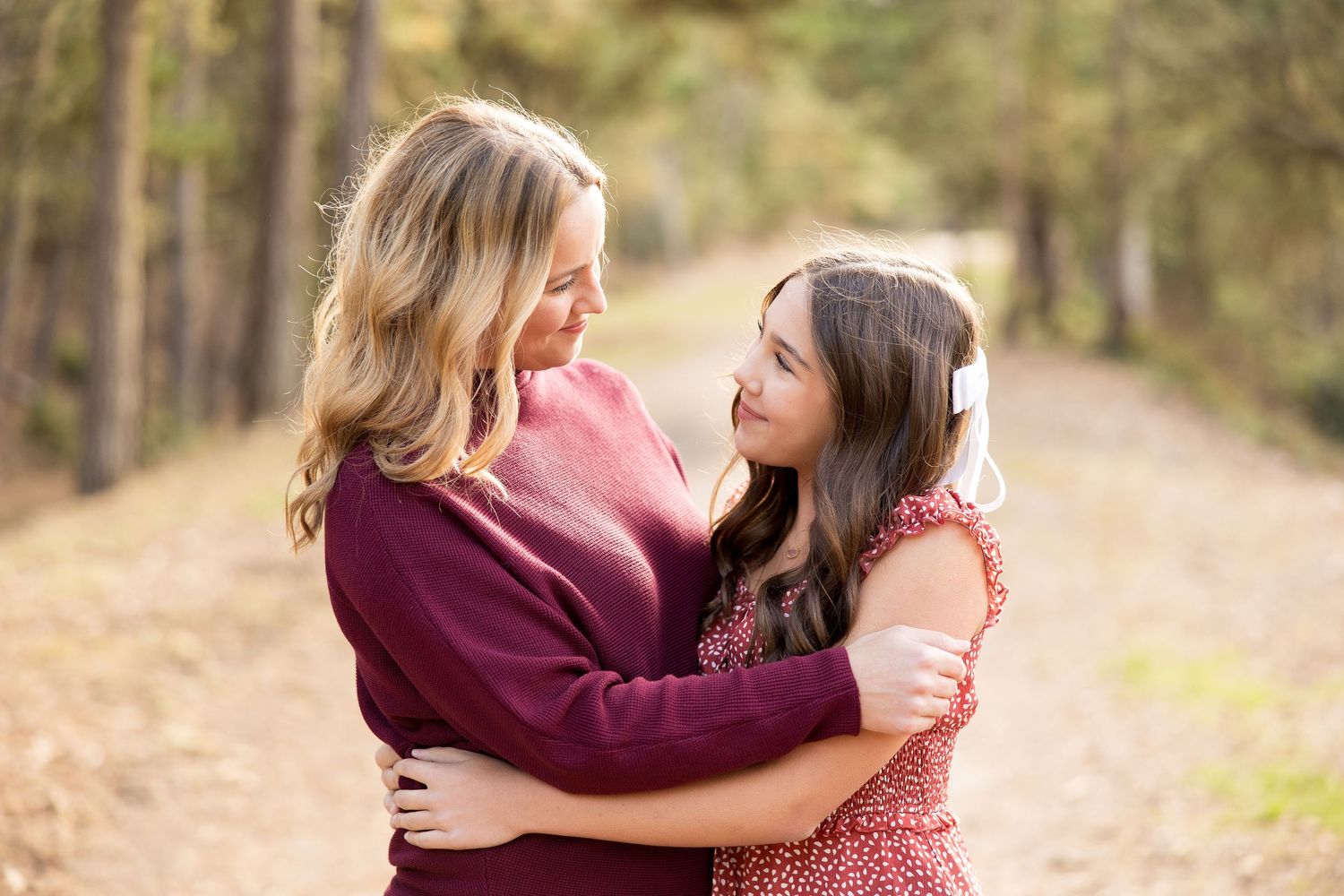 Two people embrace warmly while standing on a sunlit forest path.