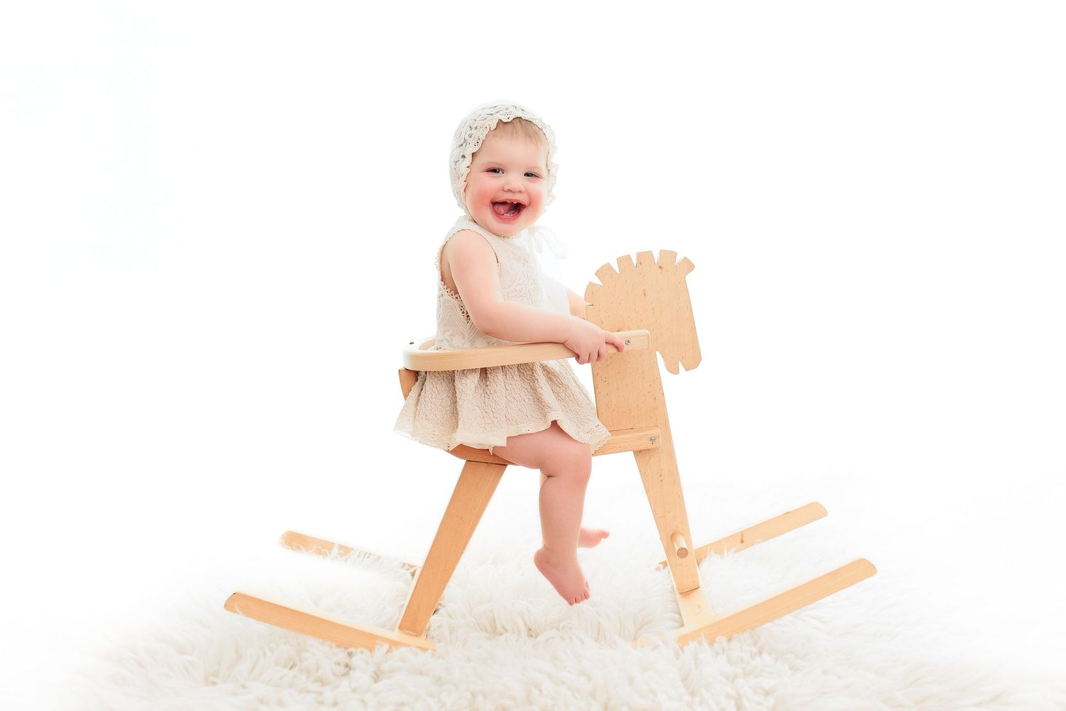 Baby playing on wooden rocking horse against white background.