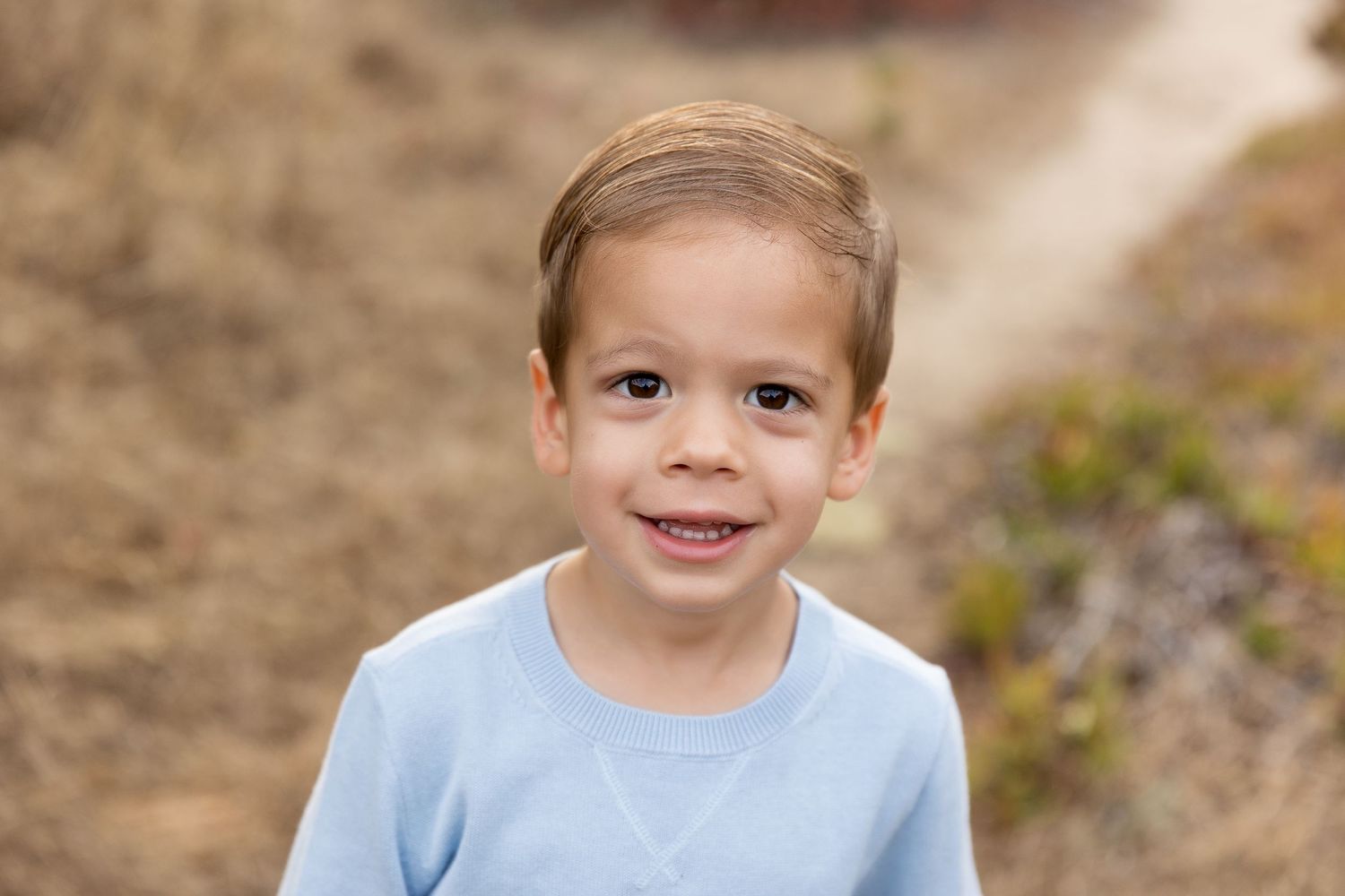 Child wearing light blue sweater poses for portrait outdoors.
