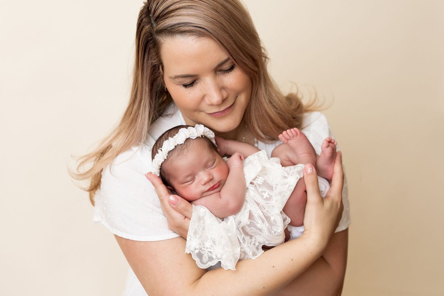 Tender moment with swaddled newborn in white lace against neutral backdrop.