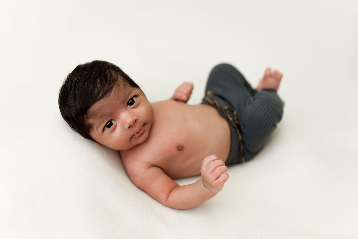 Happy baby wearing denim pants lying on white background with bright smile.