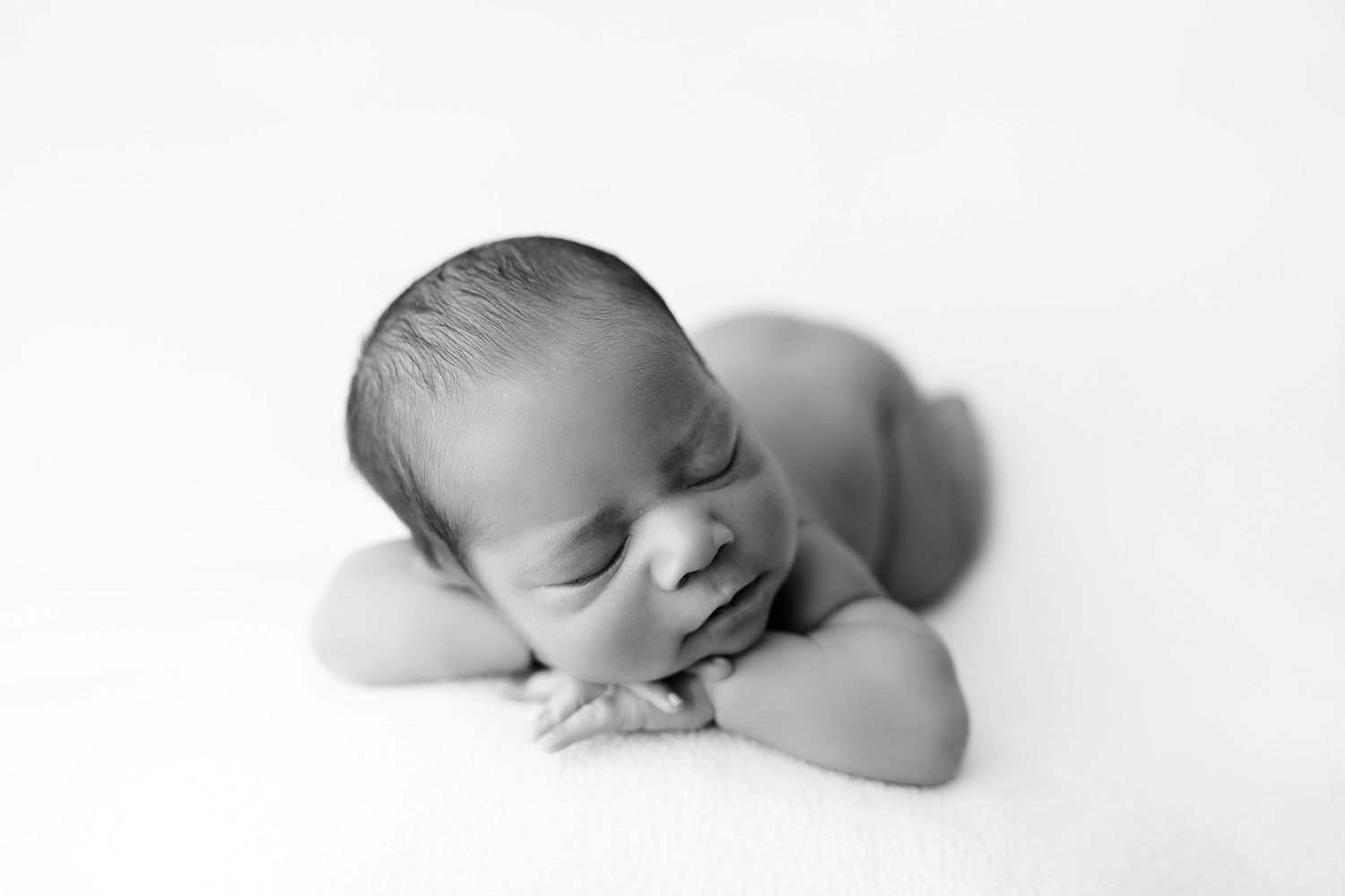 Black and white photograph of a sleeping newborn baby resting their head on crossed arms.