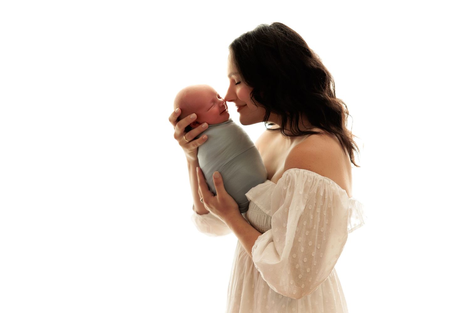Mother in white dress holding baby in silhouette against light background.