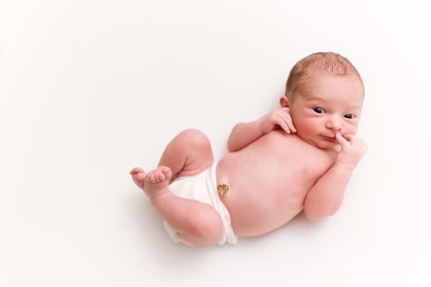 Newborn baby lying on white background with tiny arms and legs stretched out.