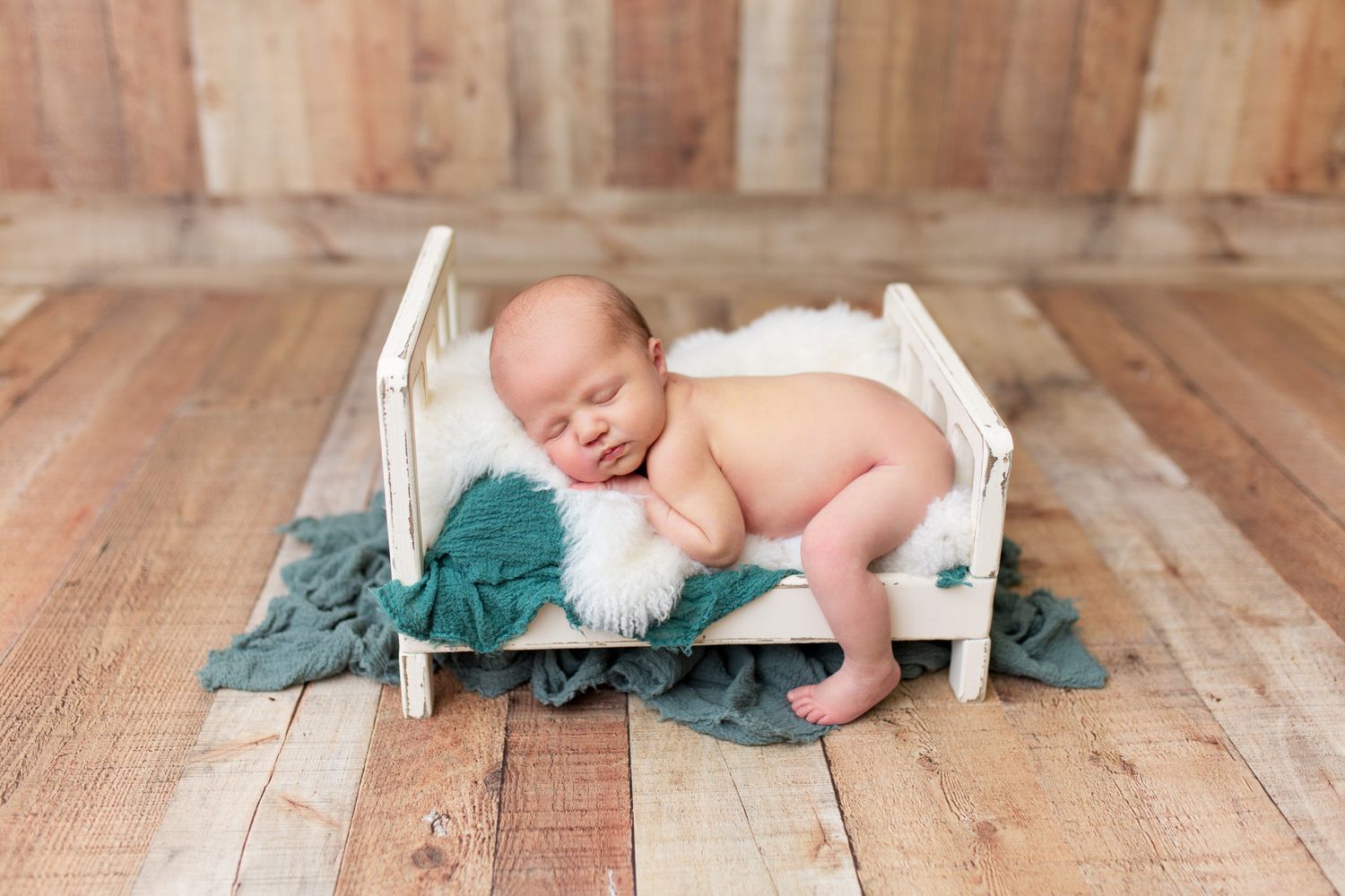 A baby crawls on a wooden floor while exploring white candles arranged in a line.