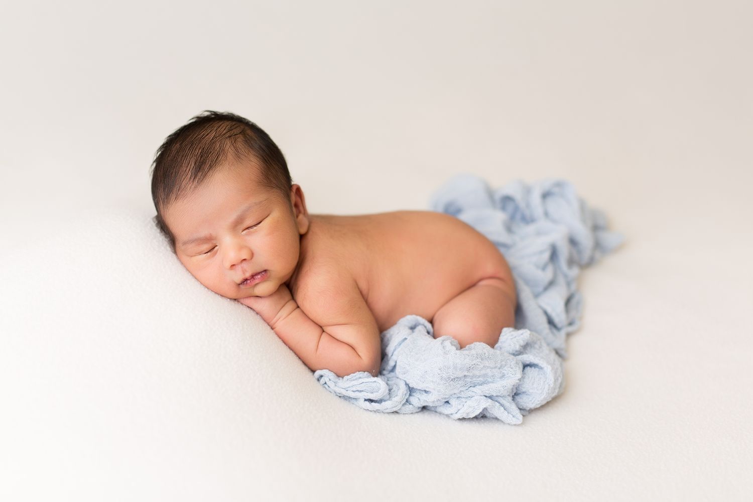 Sleeping newborn baby wrapped in soft blue fabric in multiple artistic poses on white background.