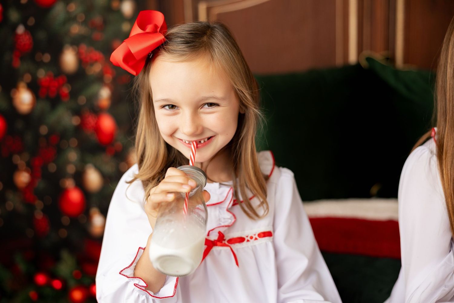Girl in white Christmas pajamas sipping milk through a striped straw at a holiday mini session in Pacific Grove