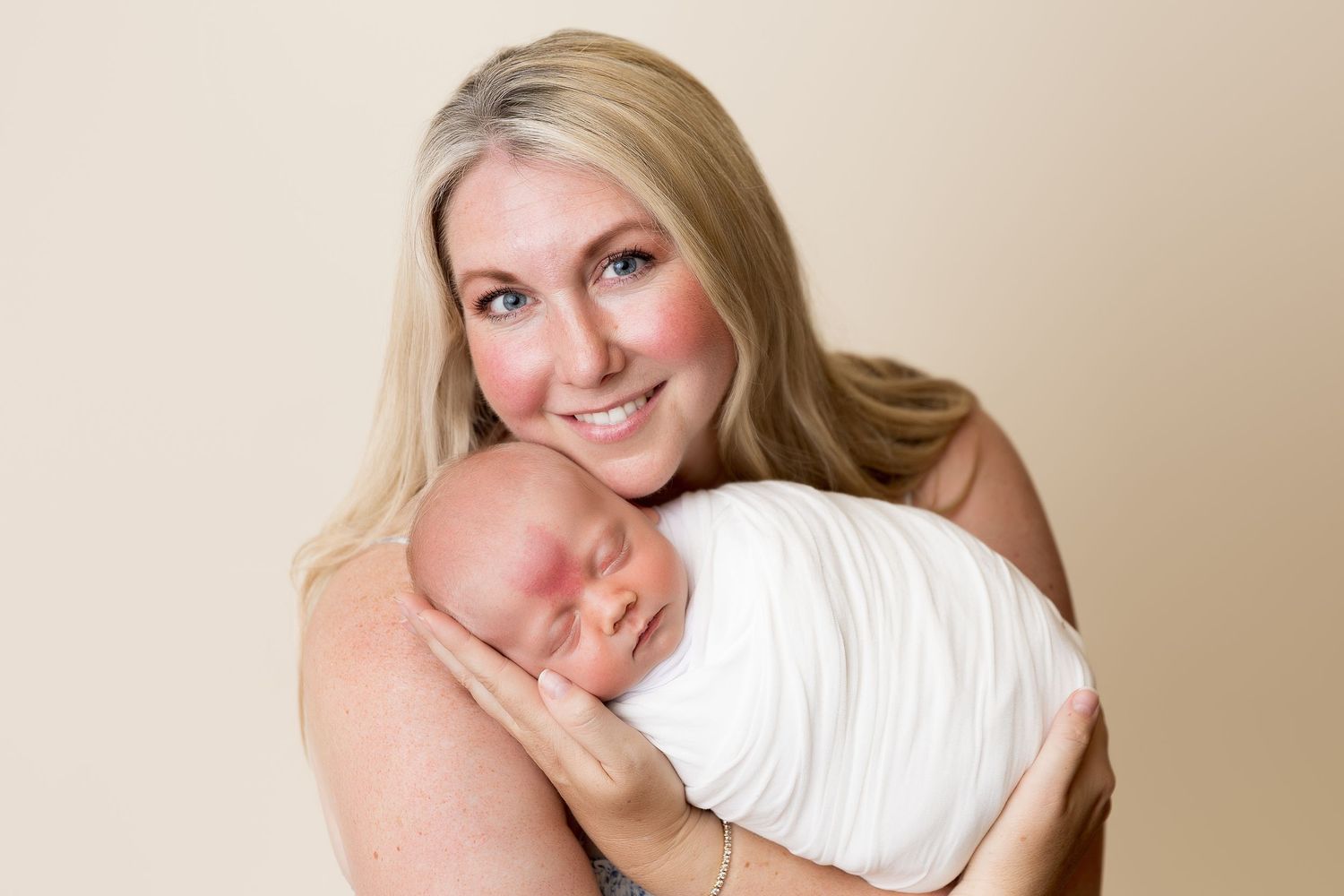 Tender moment between parent and swaddled newborn against neutral background.